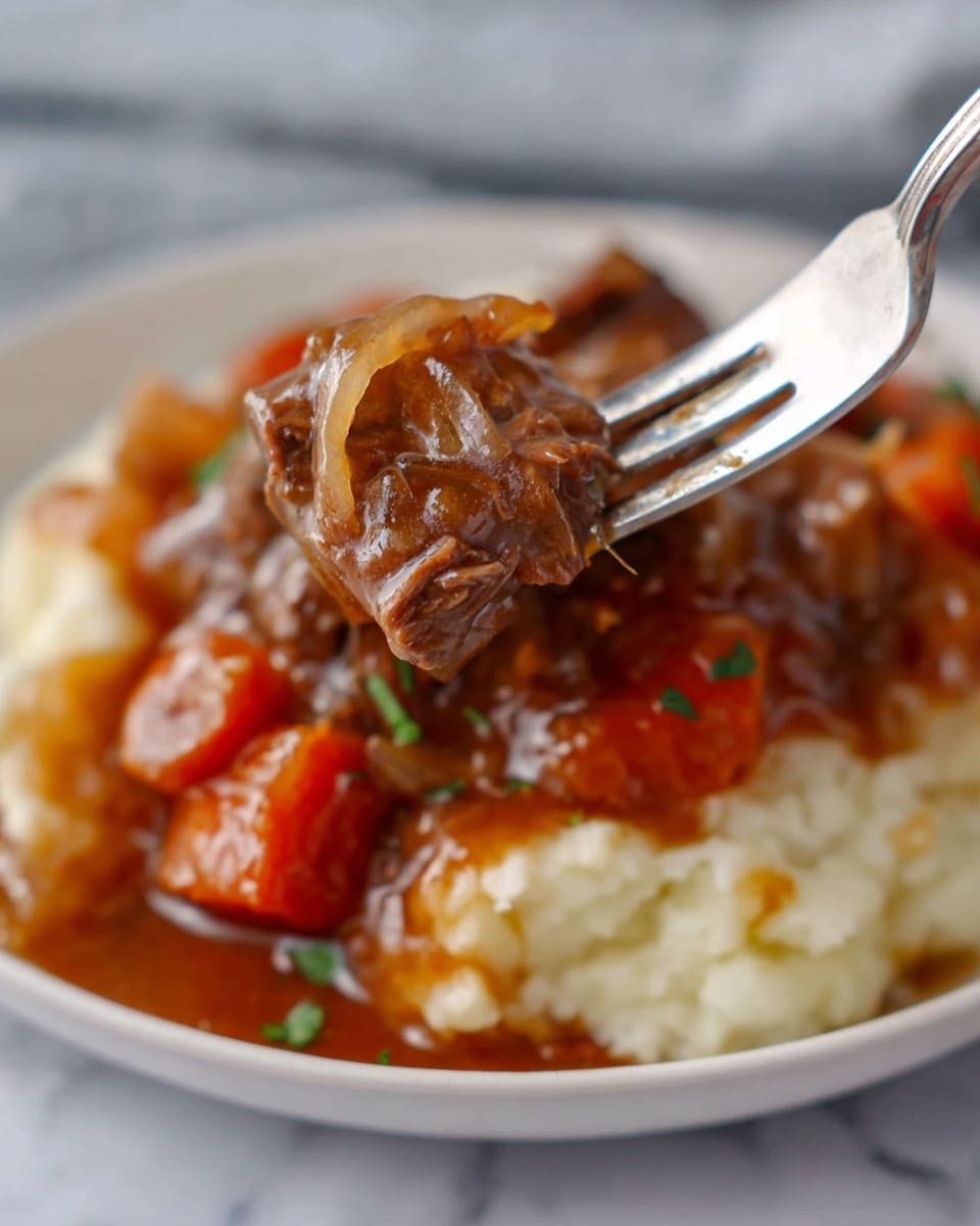 The image shows a close-up of a silver fork lifting a piece of tender beef stew with soft chunks of orange carrot and translucent cooked onions covered in rich, glossy brown gravy. Below, there is a layer of creamy, pale mashed potatoes on a white plate. Small green herb bits are sprinkled on top of the stew, adding a touch of fresh color. The background is a white marbled surface, giving a clean and bright feel to the scene. Photo taken with an iphone --ar 4:5 --v 7