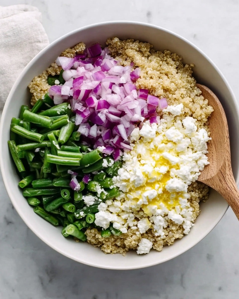 A white bowl sits on a white marbled surface, filled with three main layers arranged side by side. The bottom layer is a tan, grainy quinoa base covering the entire bowl. On top, the left side is bright purple and white chopped onions, the middle shows bright green chopped green beans, and the right side is topped with white crumbled cheese with a drizzle of yellow oil on it. A wooden spoon rests on the right edge of the bowl, partially in the cheese layer. Photo taken with an iphone --ar 4:5 --v 7