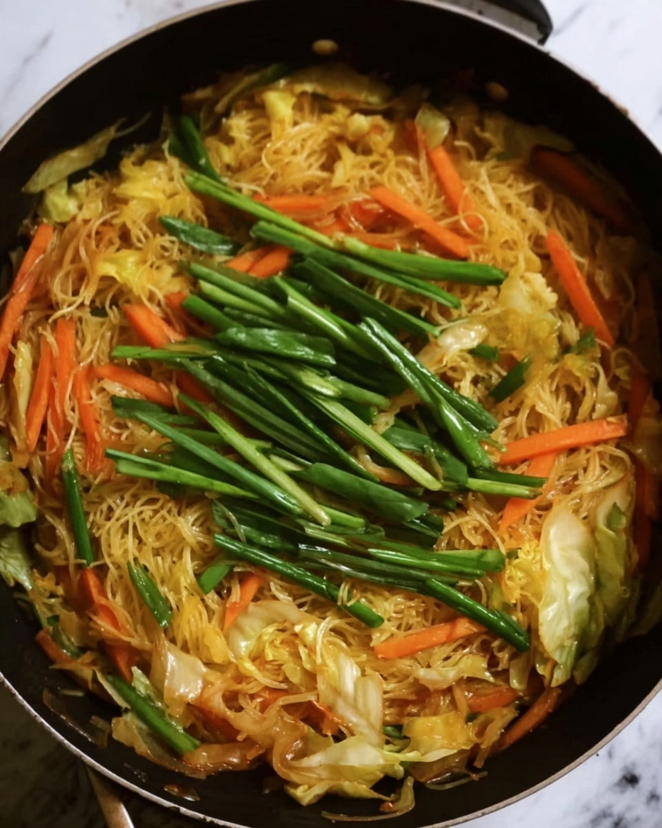 A black pan filled with cooked thin yellow noodles mixed with sliced carrots and cabbage forming the bottom layer, topped with long green onions spread across the center, all the ingredients cooked with a slightly shiny, soft texture. The background surface is a white marbled texture. photo taken with an iphone --ar 4:5 --v 7