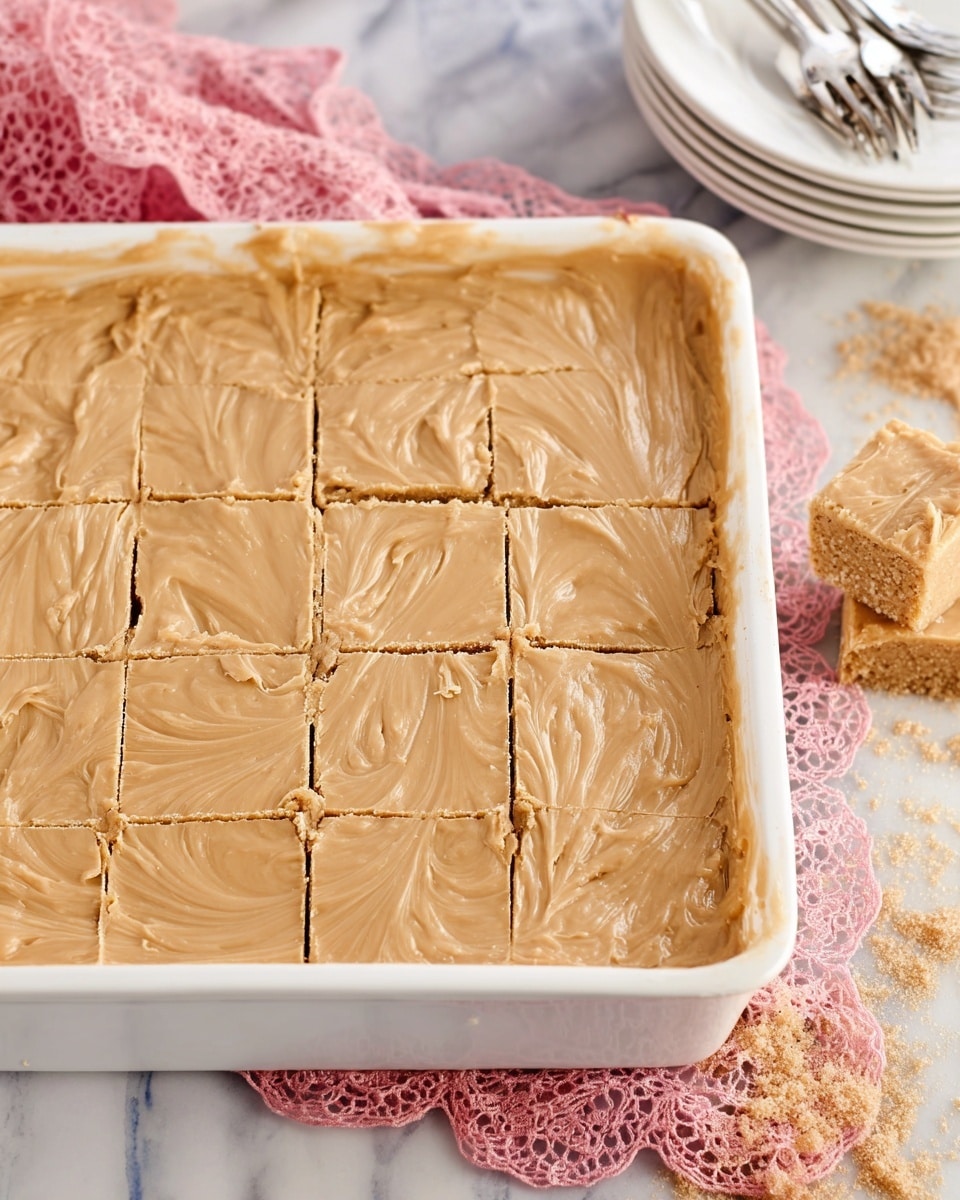 A square white baking dish filled with a creamy light brown fudge-like dessert that has been cut into 16 squares. The surface of the dessert is smooth with gentle swirling and some cracks, showing a soft but firm texture. The dish sits on a white marbled surface with a pink lace cloth partially beneath it, some brown sugar scattered to the side, and a stack of white plates with silver forks in the top right corner. Photo taken with an iphone --ar 4:5 --v 7