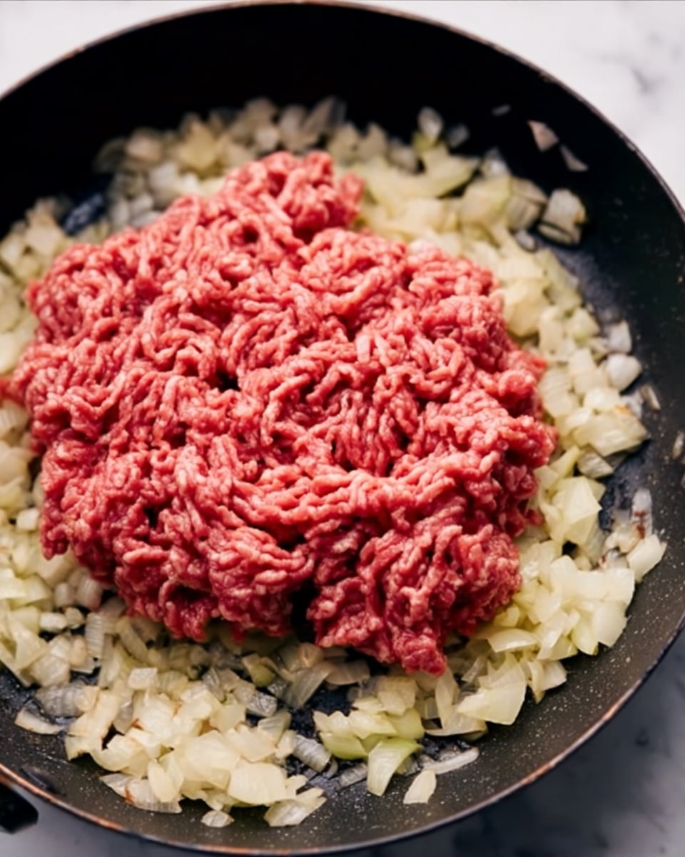 The image shows a close-up of raw ground meat with a red color placed in the middle of a pan, surrounded by chopped onions that are light golden and slightly translucent. The ground meat has a textured, stringy appearance, while the onions around it form a ring close to the edges of the pan. The pan is set on a white marbled surface. photo taken with an iphone --ar 4:5 --v 7