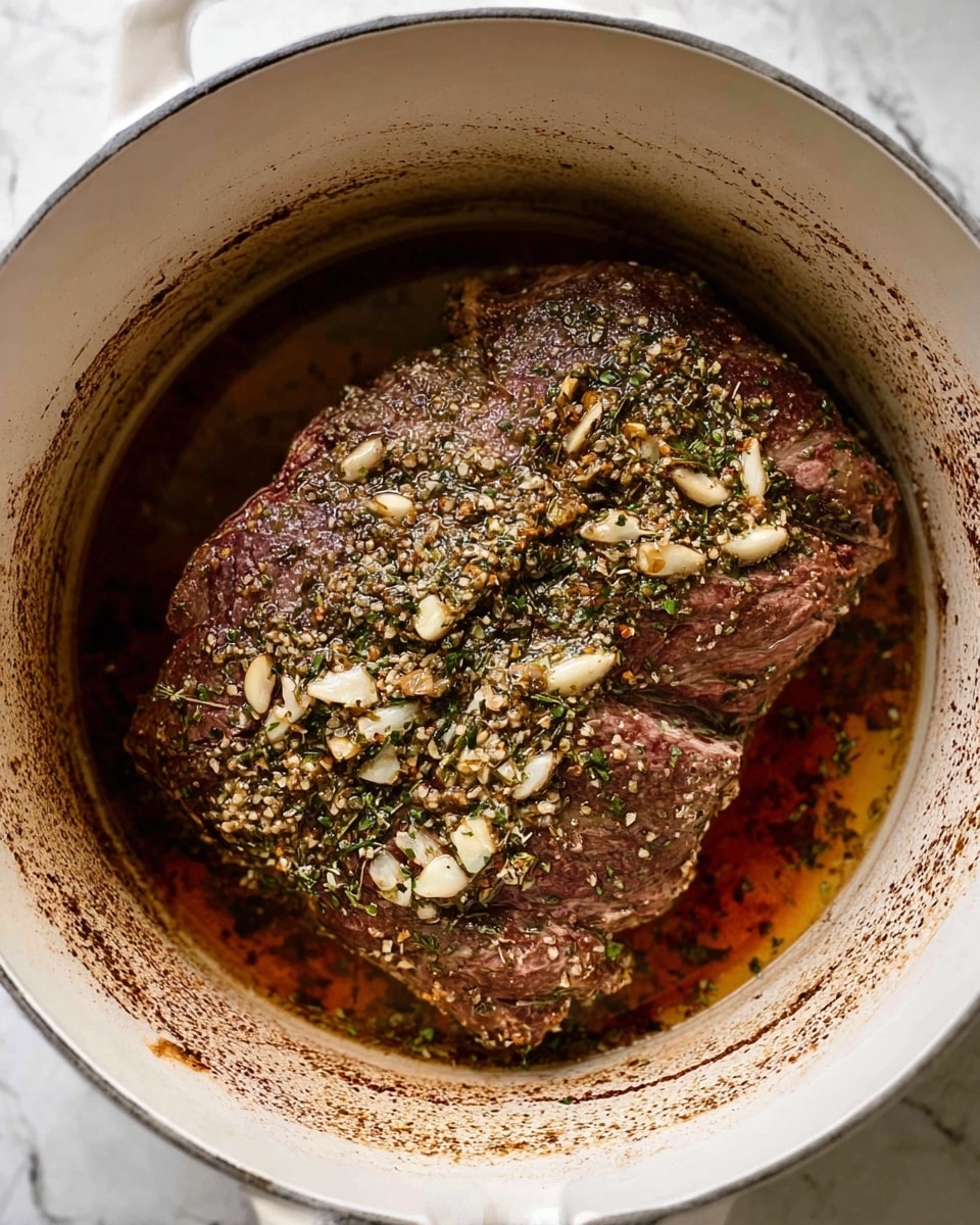 A large piece of meat covered with small pieces of garlic and green herbs, sitting in a white pot with a small amount of brown cooking juice around it; the meat is dark brown with a slightly textured surface, and the inside of the pot has some brown stains from cooking, all placed on a white marbled surface photo taken with an iphone --ar 4:5 --v 7