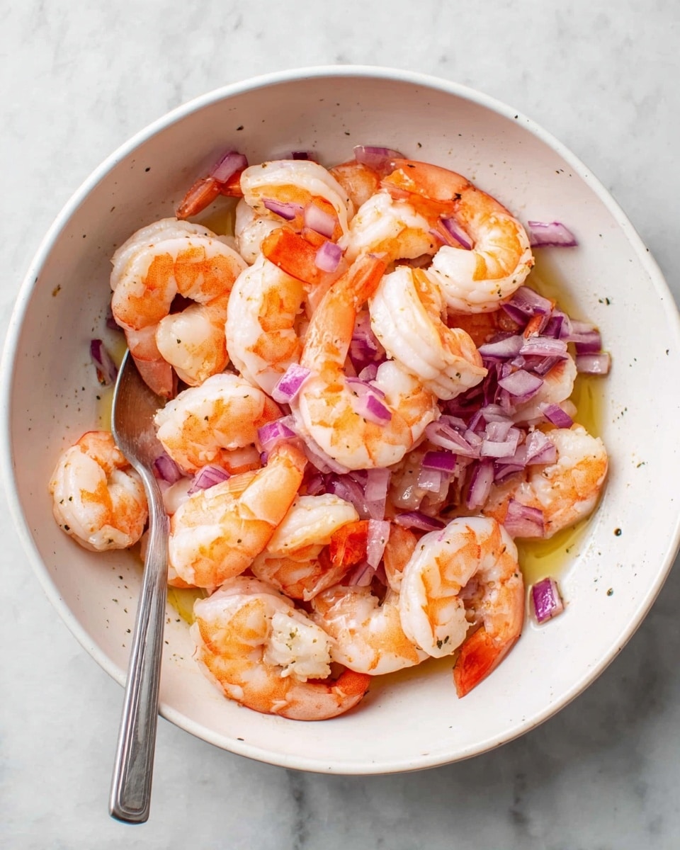 In a white bowl on a white marbled surface, there is a mix of cooked shrimp and chopped red onions. The shrimp are bright orange with a slightly translucent white inside, arranged loosely in the bowl. Scattered among the shrimp are small pieces of purple-red onion, adding a touch of color contrast. A spoon is placed inside the bowl, resting on the edge. The bowl has some light olive oil coating the bottom, giving a slight shine to the shrimp and onions. Photo taken with an iphone --ar 4:5 --v 7