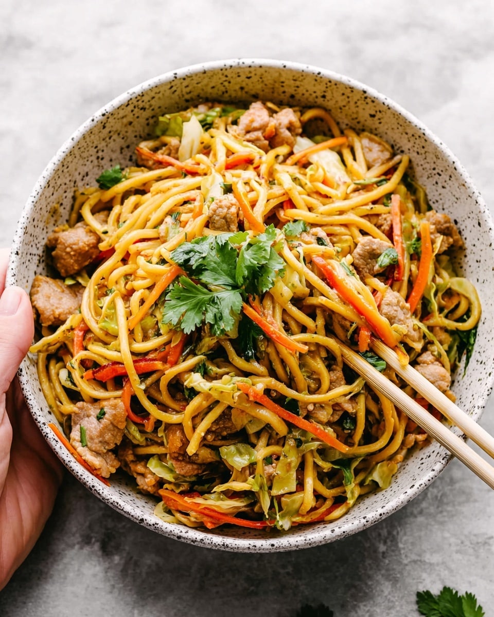 A bowl filled with yellow noodles mixed with small chunks of light brown cooked meat scattered evenly throughout. Thin strips of orange carrots and light green cabbage are layered among the noodles. Fresh green herbs, including cilantro leaves, rest on top, adding pops of color. The bowl is white with dark speckles, held slightly by a woman's hand, and rests on a white marbled surface. A pair of light-colored chopsticks is placed on the edge of the bowl, reaching into the noodles. photo taken with an iphone --ar 4:5 --v 7