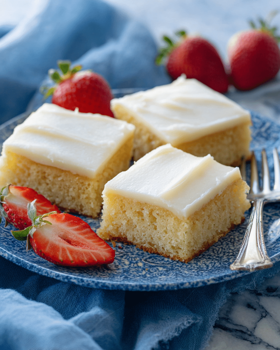 The image shows three square pieces of a two-layer dessert on a white plate. Each piece has a bottom layer of light golden cake with a soft, crumbly texture, topped with a smooth, creamy white frosting layer. One piece in the front center is decorated with three thin, overlapping slices of bright red strawberries. In the background, there are three whole strawberries with green tops. A small silver fork is placed on the right side of the plate, which rests on a white marbled surface. Photo taken with an iphone --ar 4:5 --v 7