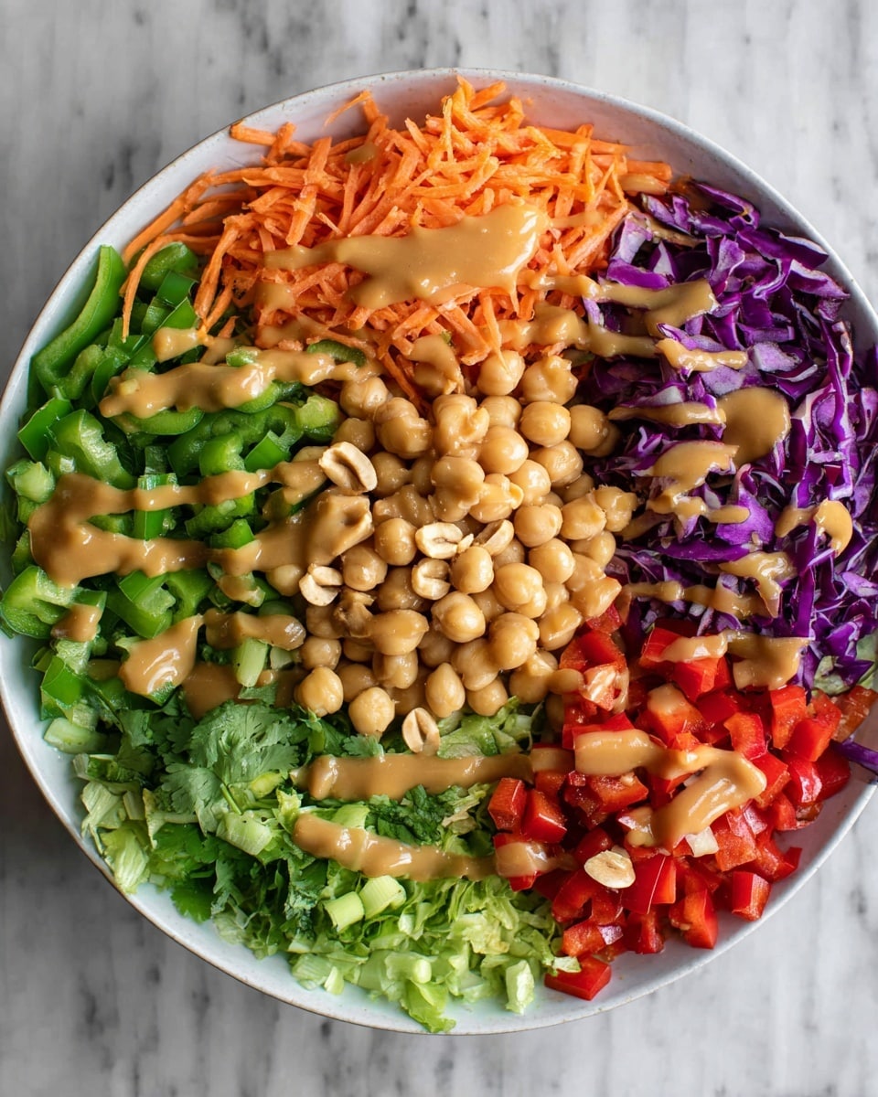 A white bowl sits on a white marbled surface, filled with seven separate layers of colorful ingredients arranged neatly: shredded orange carrots on the top left, chopped green bell peppers next to them, finely chopped deep purple cabbage on the top right, light green chopped lettuce on the far right, round beige chickpeas with a drizzle of creamy light brown sauce below the cabbage and lettuce, light brown roasted peanuts with sauce centrally placed between the chickpeas and green bell pepper, and bright red diced bell peppers with chopped green onions and cilantro at the bottom left. The creamy sauce is gently drizzled over the green bell peppers, purple cabbage, peanuts, and chickpeas. Photo taken with an iphone --ar 4:5 --v 7