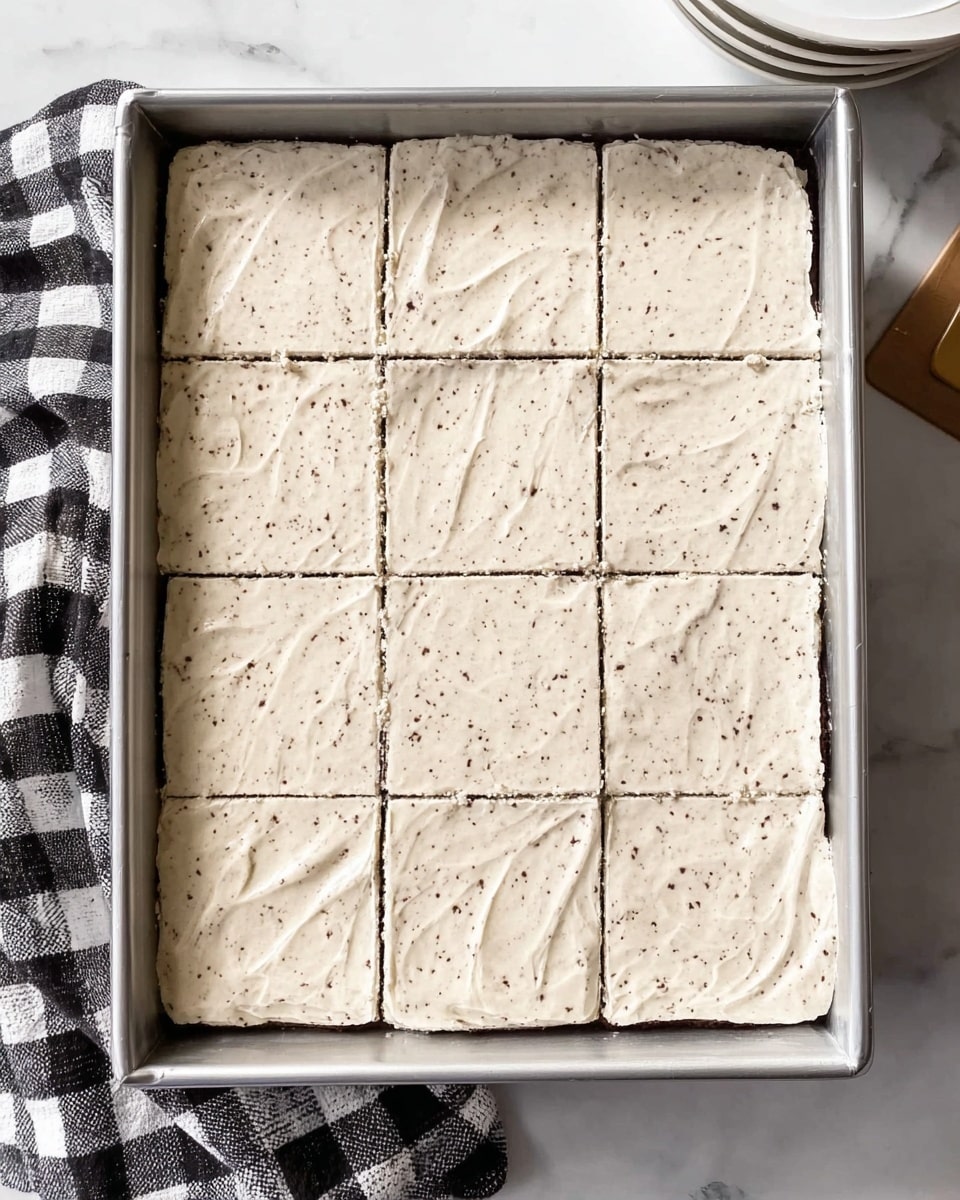 The image shows a large rectangular metal baking tray filled with a dessert that is evenly cut into 15 square pieces. The dessert has one visible layer of light cream color with small dark specks all over, giving it a textured look. The top surface of the dessert is smooth with some small lines and swirls, suggesting it was spread gently. The tray is placed on a white marbled surface, with a black and white checkered cloth partially under it on the left side. On the top right corner, there is a stack of white plates. photo taken with an iphone --ar 4:5 --v 7