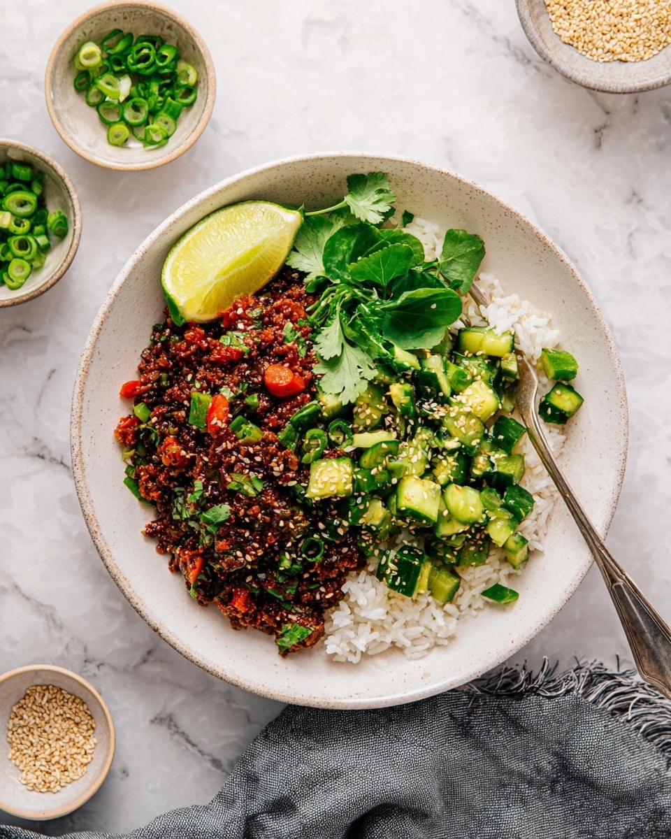 A white bowl with a layer of white cooked rice at the bottom is topped with two main parts: on the left, a dark brown textured mix that includes small pieces of red bell pepper and chopped green herbs, sprinkled lightly with sesame seeds, and on the right, chopped cucumber pieces mixed with green onions and a light dressing, also sprinkled with sesame seeds. A bright lime wedge and fresh green leaves sit on top near the center, adding color. A silver fork rests on the right side of the bowl, which is placed on a white marbled surface, with small bowls of green onions and sesame seeds nearby, and a gray cloth partially visible below. Photo taken with an iphone --ar 4:5 --v 7