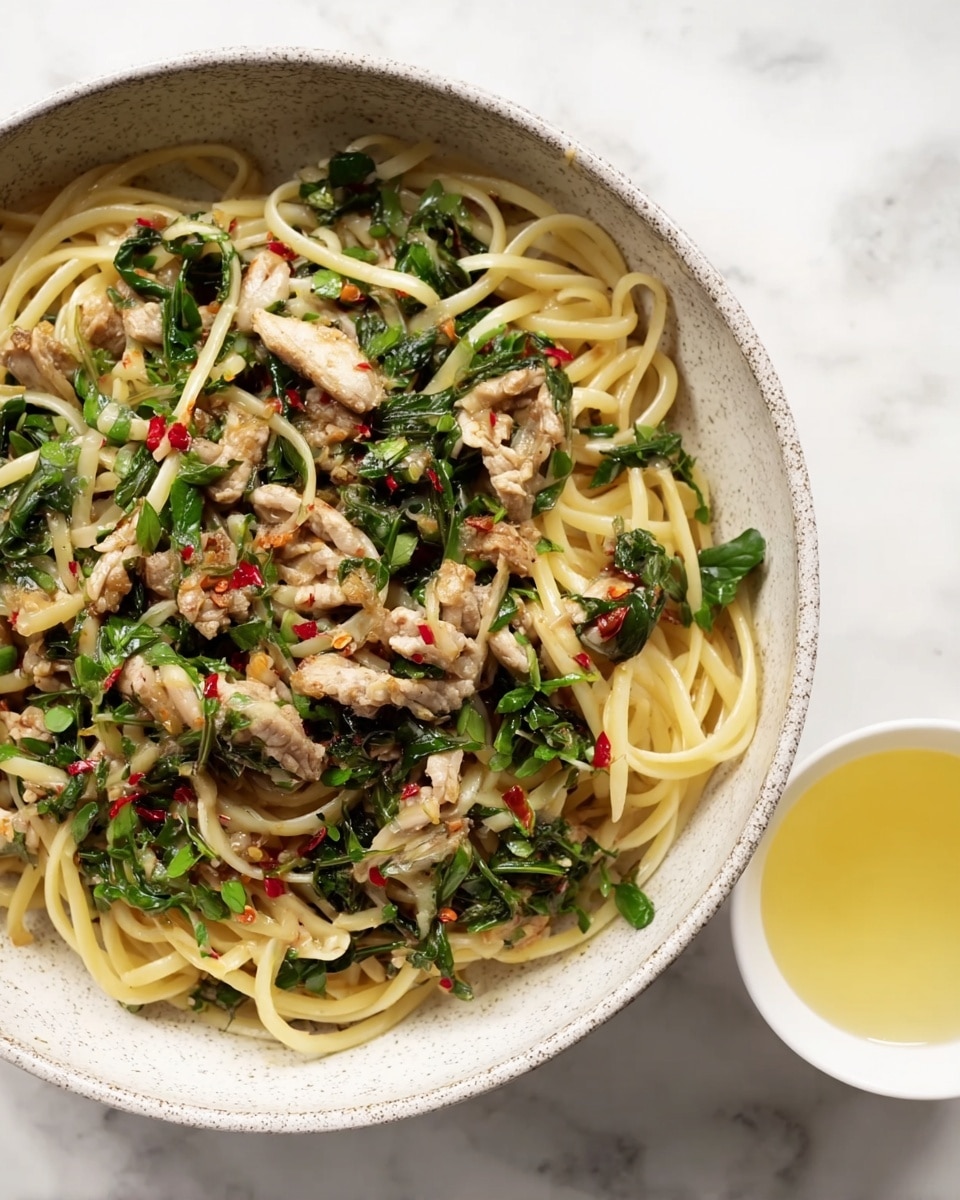 A white speckled bowl holds a dish with three main layers: the first layer is long, pale yellow pasta noodles that are glossy and intertwined across the bowl; the second layer consists of pieces of cooked, light brown meat scattered evenly among the noodles; the third layer includes bright green leafy vegetables mixed throughout, with small bits of red chili flakes and chopped herbs sprinkled on top for color and texture. To the right of the bowl, there is a small white cup filled with pale yellow liquid on a white marbled surface. photo taken with an iphone --ar 4:5 --v 7