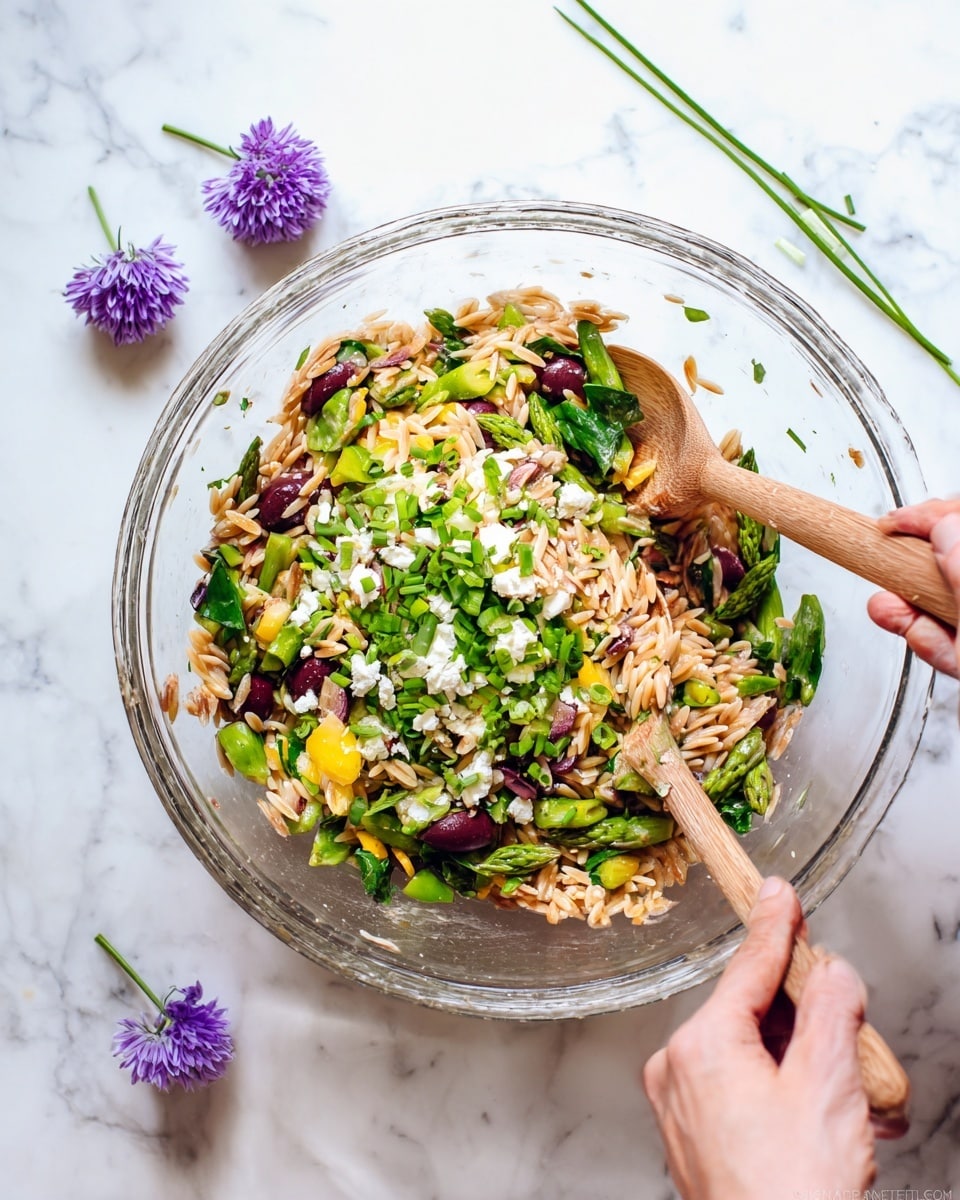 A clear glass bowl filled with a colorful salad sits on a white marbled surface. The salad has layers that include light brown toasted orzo pasta spread all over, bright green chopped asparagus and spinach leaves mixed in, dark purple sliced olives scattered throughout, and small white chunks of cheese sprinkled on top. There are also pieces of yellow bell pepper and finely chopped green chives visible around the edges. Two wooden spoons held by a woman's hand and a hand are mixing the salad in the bowl. In the background, there are three small purple flowers with green stems lying on the white marbled surface. photo taken with an iphone --ar 4:5 --v 7