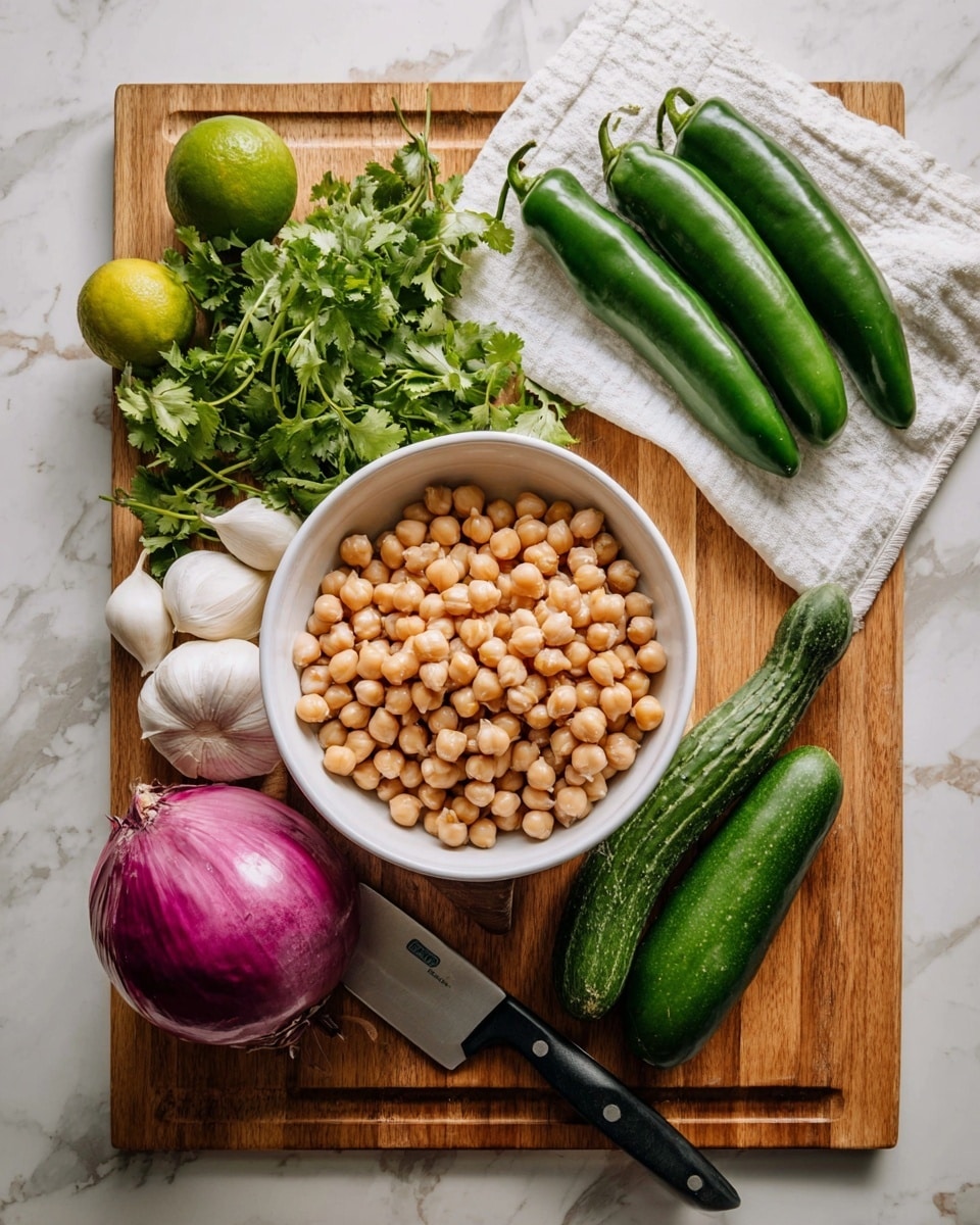 A white bowl filled with two kinds of beans, mostly light brown chickpeas layered on top of white beans, sits in the center of a wooden cutting board. Around the bowl, there are three fresh green chili peppers in a row, a large purple onion, a bunch of fresh green cilantro placed on a white cloth with a black-handled knife beside it. On the left side of the board are two green limes, several white garlic cloves, and a long dark green cucumber. The whole setup rests on a white marbled surface photo taken with an iphone --ar 4:5 --v 7
