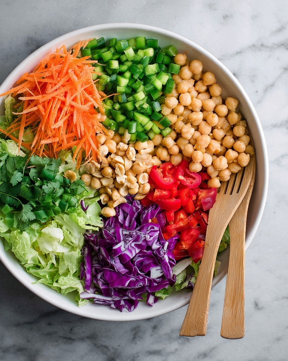 A white bowl filled with seven sections of fresh ingredients arranged in a circular pattern, starting with shredded orange carrots, diced green bell peppers, chopped purple cabbage, chopped green lettuce, whole roasted peanuts, chickpeas, and diced red bell peppers. There are also small bunches of cilantro and sliced green onions layered near the red bell peppers. Two light brown wooden salad forks rest on the right side of the bowl on a white marbled surface. photo taken with an iphone --ar 4:5 --v 7