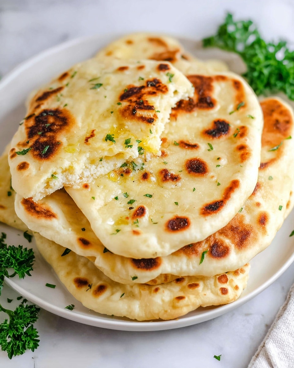 The image shows a white plate with five pieces of flatbread stacked on top of each other. The flatbreads are round with uneven edges and have a light golden color with darker brown toasted spots scattered across their surfaces. The top flatbread is partially torn, revealing a soft, fluffy inside with a melted butter-like shine and small green parsley bits on it. The plate sits on a white marbled surface with green parsley leaves placed around the plate for decoration. Photo taken with an iphone --ar 4:5 --v 7