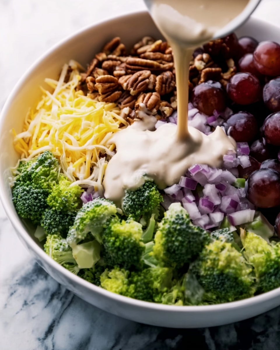A white bowl holds a colorful salad arranged in separate sections, showing a variety of fresh foods. Starting from the bottom left, there are bright green broccoli florets with a rough texture. Above the broccoli, small pieces of chopped red onion add a purplish-pink color and a slightly translucent texture. To the right of the broccoli, there are dark purple grapes with a smooth, shiny surface. Just above the grapes, shredded yellow cheese adds a soft, thin layer. At the top of the bowl, a group of brown pecan nuts provides a rough, bumpy texture. In the center, a creamy beige sauce with a smooth surface is being poured, slightly covering the edges of the other ingredients. The bowl sits on a white marbled surface. photo taken with an iphone --ar 4:5 --v 7