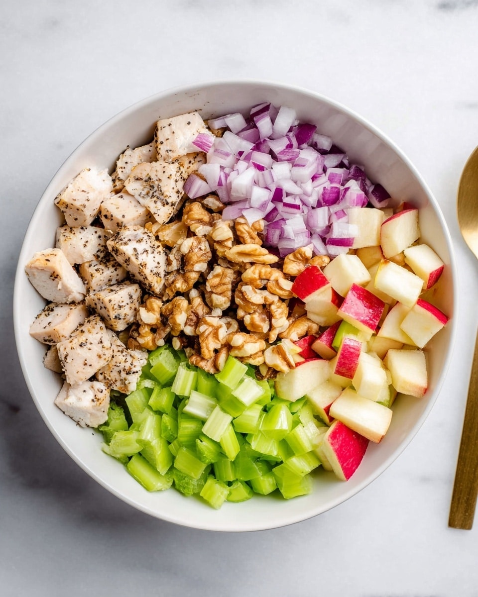 A white bowl sits on a white marbled surface filled with five separate layers of food. On one side, there are pieces of cooked chicken with black pepper, light beige with a slightly charred texture. Next to it is a layer of small chopped red onions with light purple and white colors. Beside that, there is a bright green layer of chopped celery with a fresh and crisp look. In the middle, there is a pile of light brown walnut pieces with a rough texture. The last layer is made up of small chopped red and green apples with shiny skin and pale flesh. A gold spoon is partly visible on the right side of the image. photo taken with an iphone --ar 4:5 --v 7
