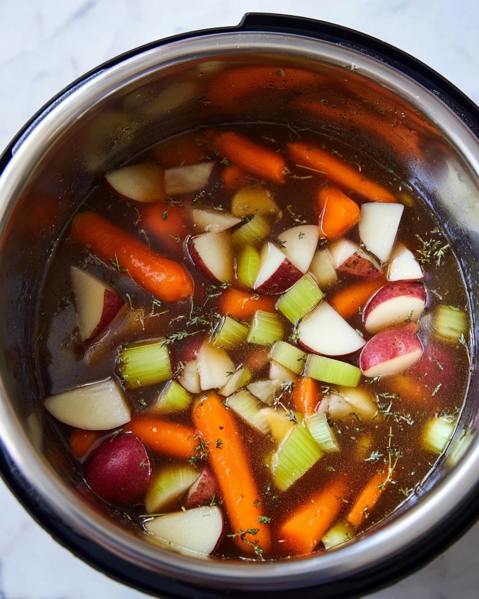 Inside a shiny silver pot, there is a mix of chopped vegetables and broth. The bottom layer is a dark brown broth with visible herbs spread evenly. Floating on top, there are thick slices of bright orange carrots, chopped pale green celery, white onion pieces, and chunks of red-skinned potatoes with white inside. The colors contrast well against the shiny silver pot's smooth inner surface. The image is set on a white marbled texture. photo taken with an iphone --ar 4:5 --v 7