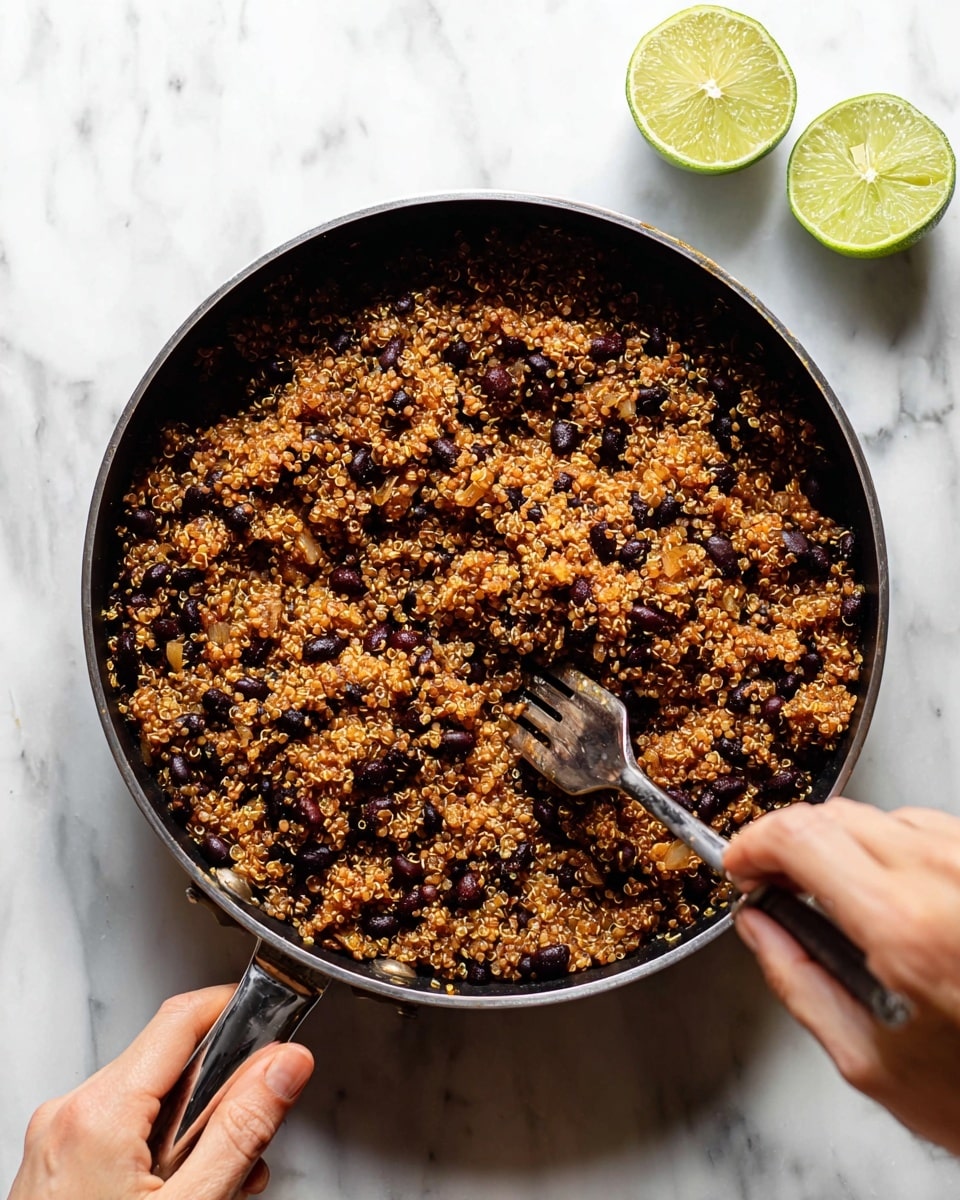 A black pan filled with one layer of cooked quinoa mixed with black beans and small pieces of cooked onion, giving a reddish-brown color with bits of dark brown and light amber mixed in. A woman's hand is holding the pan handle on the left, and another woman's hand is stirring the mix with a fork in the pan. The pan is placed on a white marbled surface. Two squeezed lime halves are placed above the pan. photo taken with an iphone --ar 4:5 --v 7