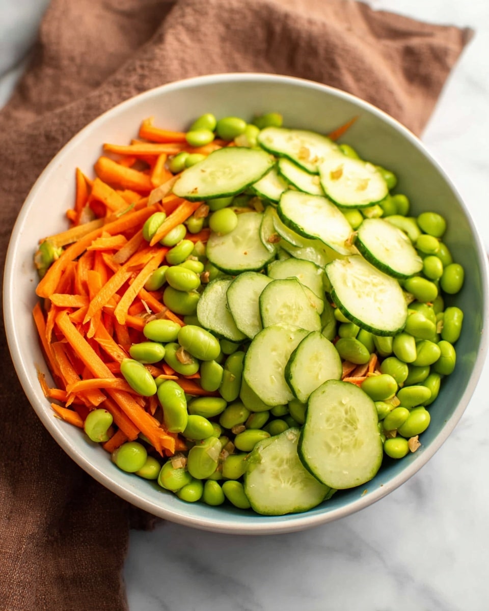 A white bowl filled with three layers of vegetables: the bottom layer is bright green edamame beans, the middle layer consists of thin orange carrot sticks spread evenly, and the top layer has light green cucumber slices with dark green edges placed on top. The bowl sits on a white marbled surface with part of a brown cloth visible in the background. Photo taken with an iphone --ar 4:5 --v 7
