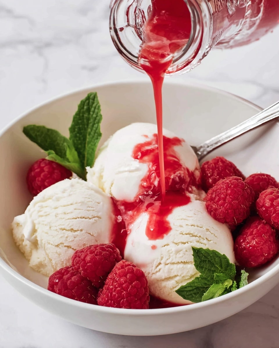 In a white bowl, three scoops of creamy white vanilla ice cream form the bottom layer, with smooth, slightly textured surfaces visible. Bright red raspberries are scattered between the scoops, adding a juicy, bumpy texture and vibrant color contrast. On top of the ice cream, a clear glass bottle pours a bright red syrup that drizzles over the scoops, creating a glossy, flowing effect. Fresh green mint leaves sit beside the raspberries, adding a pop of fresh color. The bowl rests on a surface with a white marbled texture, and a silver spoon is partially visible behind the ice cream. photo taken with an iphone --ar 4:5 --v 7