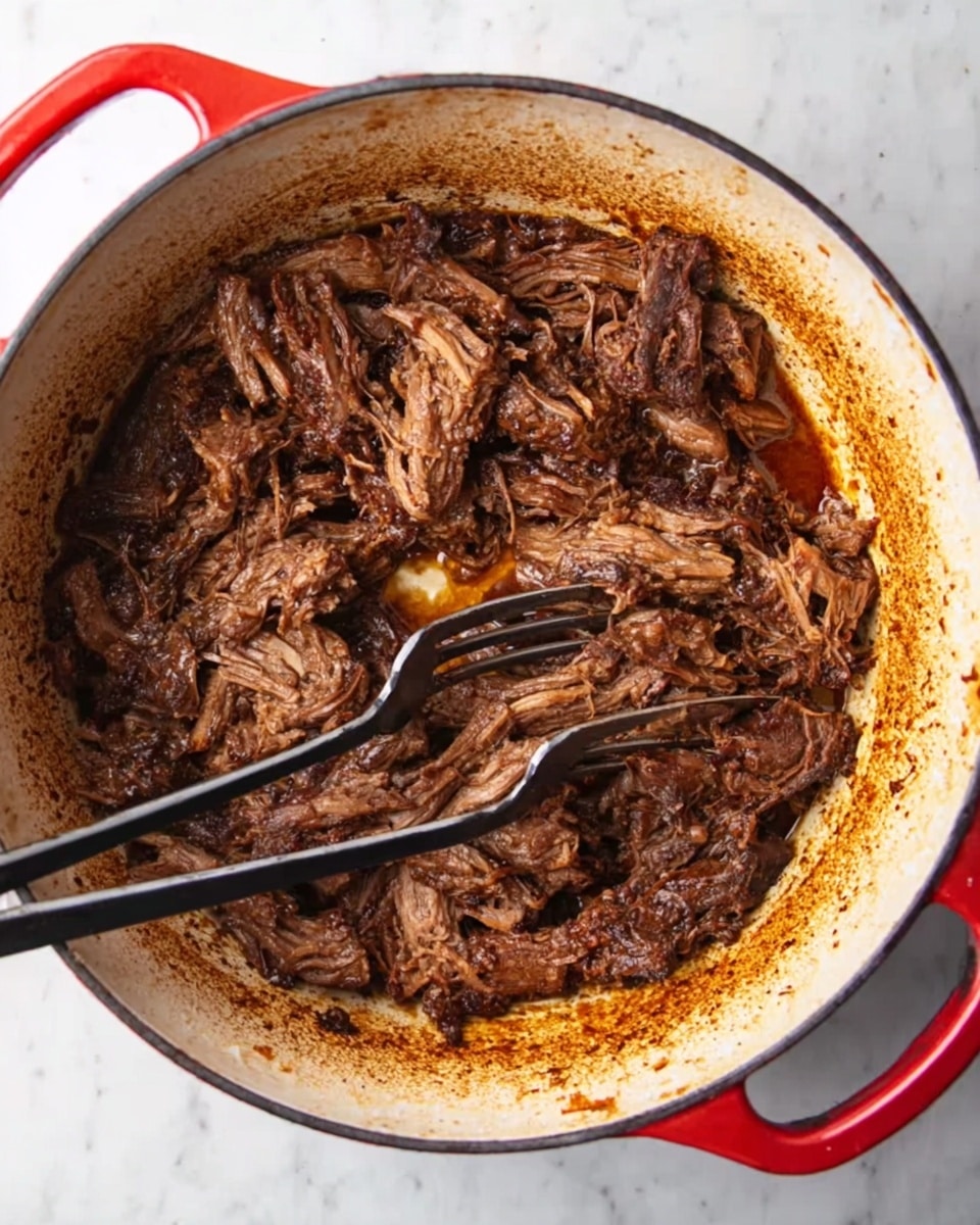 A round white pot with red handles is filled with shredded dark brown cooked meat in thick brown sauce. Two black forks are placed inside the pot, positioned near the center, gently pulling apart the tender meat. The inside of the pot shows some browning and sauce stains, and the pot sits on a white marbled surface. photo taken with an iphone --ar 4:5 --v 7