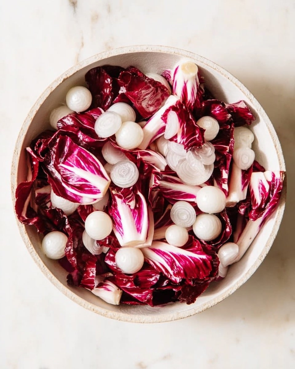 A white bowl filled with pieces of deep red and white striped radicchio leaves layered with small, round white onions scattered evenly throughout the bowl, all placed on a white marbled surface. The vibrant red leaves have smooth, slightly crinkled textures, and the onions add a smooth, glossy contrast. photo taken with an iphone --ar 4:5 --v 7