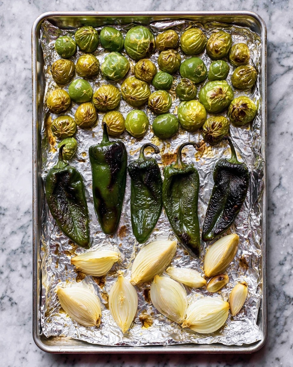 A silver baking sheet lined with crinkled foil sits on a white marbled surface, holding three groups of roasted vegetables arranged in rough rows. At the top, there is a scattered layer of small, round, green tomatillos with browned, slightly charred tops, showing different shades of green turning golden. Below them, five dark green poblano peppers lay side by side, their surfaces wrinkled and blistered from roasting. At the bottom, three large, pale onion wedges and a few cloves of soft, browned garlic are spread out, their creamy white and golden edges contrasting with the green peppers and tomatillos. The entire scene shows a mix of roasted textures and colors, with the foil reflecting light subtly. photo taken with an iphone --ar 4:5 --v 7