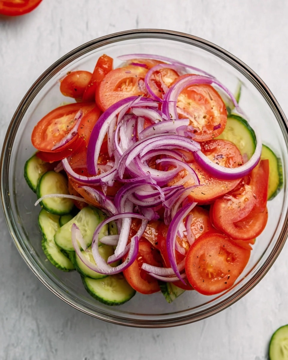 In a clear glass bowl, there is a fresh salad made of three main layers. The bottom layer shows bright green cucumber slices arranged loosely. On top of that, there are several large, thick tomato wedges, bright red with juicy texture. The top layer is made up of thin rings of purple-red onion, scattered over the tomatoes. The bowl sits on a white marbled surface, with parts of a cucumber slice and a red tomato visible around it. Photo taken with an iphone --ar 4:5 --v 7