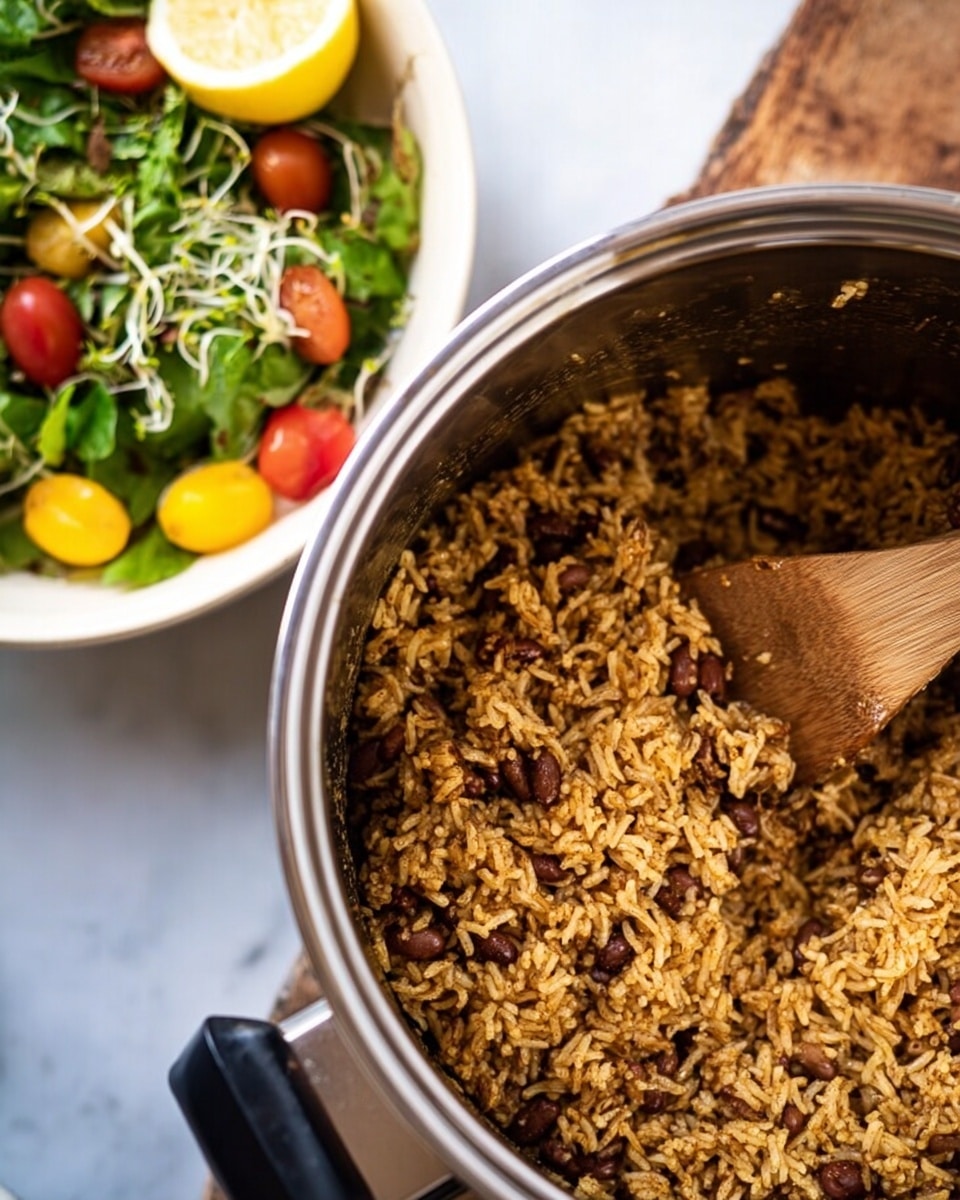 The image shows a close-up of a stainless steel pot filled with cooked seasoned rice mixed with brown beans. The rice has a light brown color with visible texture from the spices and beans scattered throughout, creating a grainy surface. A wooden spoon is partly immersed in the rice, with some rice on it, positioned on the right side inside the pot. On the left side of the image, there is a blurred view of a white bowl containing a fresh salad with green leaves, yellow and red cherry tomatoes, lemon wedges, and sprouts on top. The whole scene is set on a white marbled surface. Photo taken with an iphone --ar 4:5 --v 7