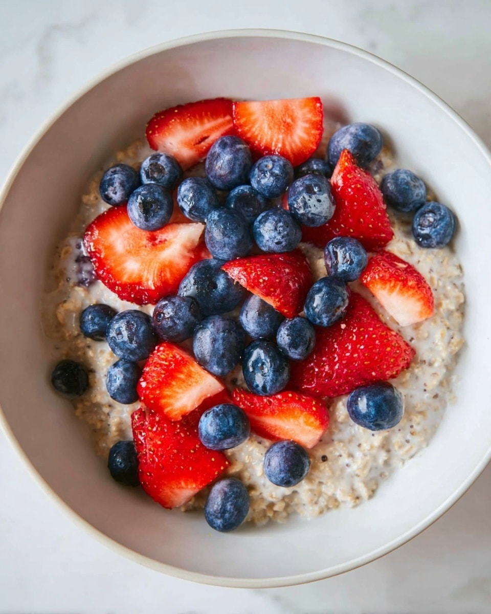 A white bowl on a white marbled surface holds a creamy chia seed pudding as the bottom layer, light beige with a slightly lumpy texture. On top, there is a thick layer of bright red sliced strawberries and plump dark blue blueberries scattered evenly. A gold spoon lies inside the bowl on the right side, with a strawberry slice resting on it. The bowl has a rustic rim with speckles, adding a natural look. photo taken with an iphone --ar 4:5 --v 7