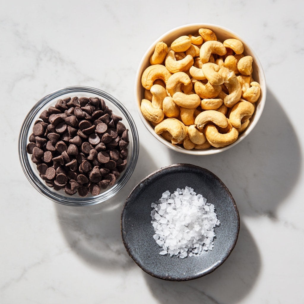 The image shows three bowls placed on a white marbled surface. On the top left, there is a clear glass bowl filled with dark brown semisweet chocolate chips, each small and rounded with a slight shine. To the right of it, there is a white bowl full of golden-brown roasted cashews, which have a smooth, curved shape and a lightly toasted color. Below these two bowls is a small, dark grey ceramic bowl containing white flaky sea salt, with the salt pieces looking coarse and irregular in shape. The light and shadows highlight the textures of the ingredients clearly. photo taken with an iphone --ar 4:5 --v 7