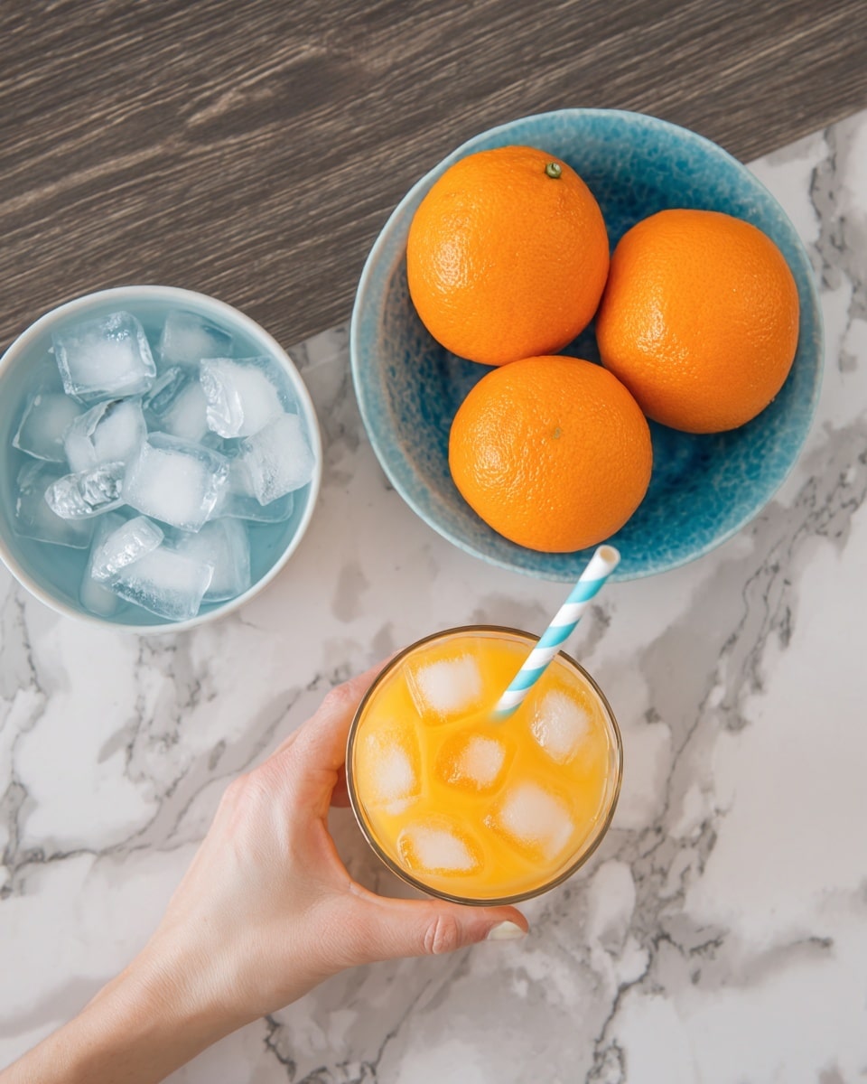 The image shows a white bowl filled with ice cubes on the left and a blue ceramic bowl with five bright orange oranges on the top right. In the lower middle, a woman's hand is holding a glass of orange juice with ice cubes and a light blue and white striped straw. Another similar glass of orange juice is placed below it, partially in view. The background is a dark wood texture with a white marbled surface underneath. Photo taken with an iphone --ar 4:5 --v 7