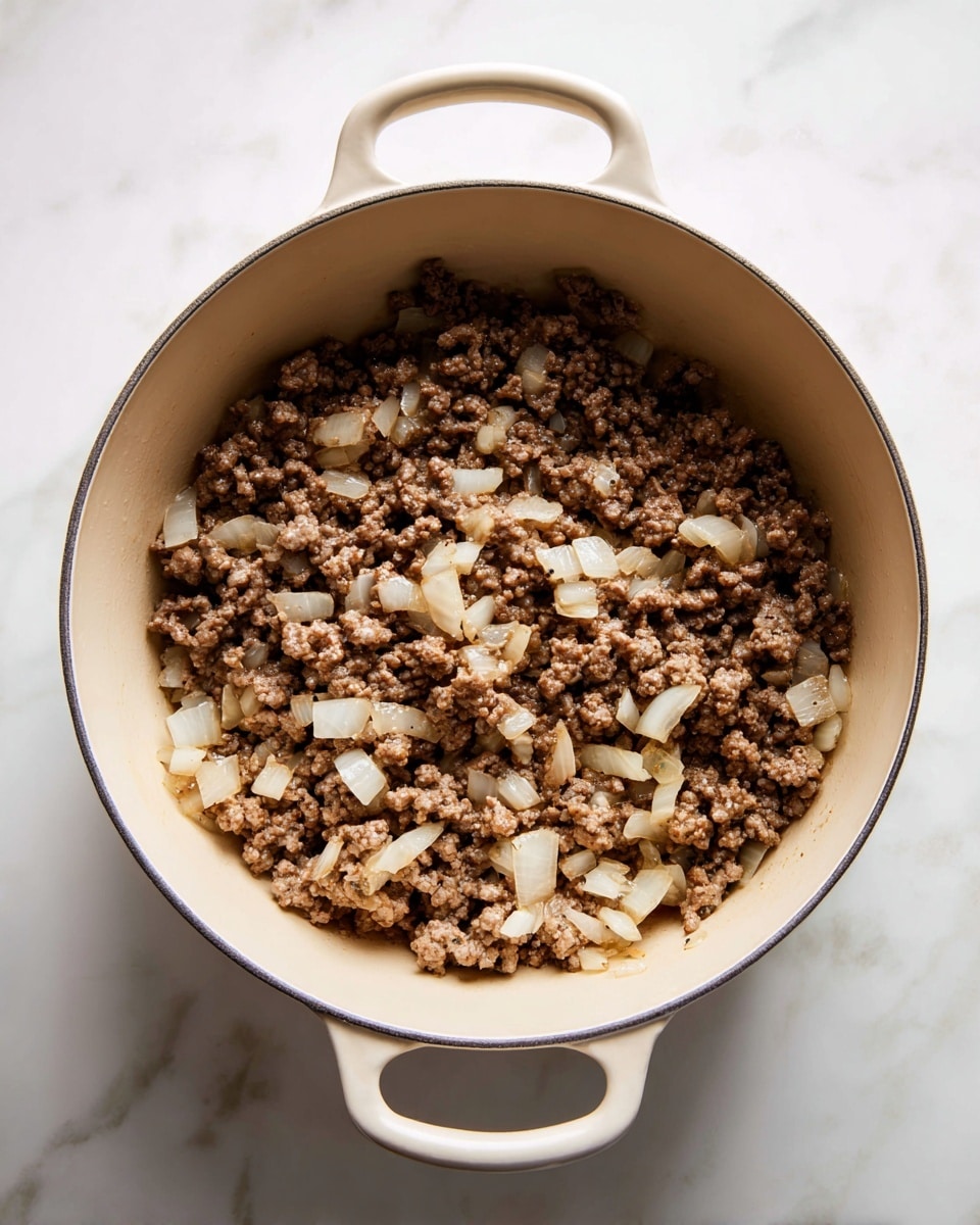 A beige cooking pot filled with cooked ground beef mixed with soft, translucent pieces of onion. The beef is brown with a crumbly texture, and the onions are cut into small uneven chunks scattered evenly throughout the meat. The pot is set on a white marbled surface, and the pot's handle is seen at the bottom center of the image. The overall lighting is soft and natural, showing details and colors clearly. photo taken with an iphone --ar 4:5 --v 7