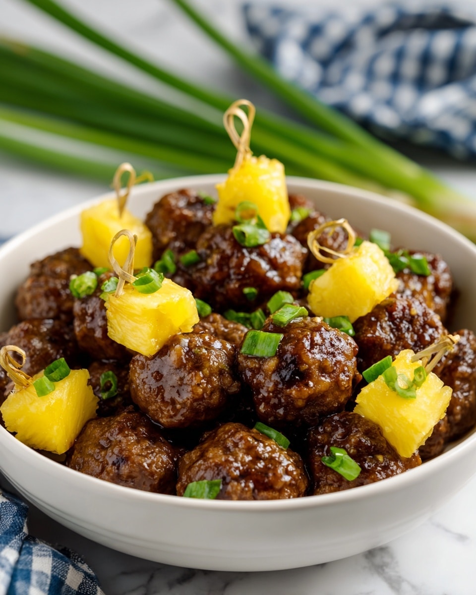 A close-up view of a white bowl full of small glossy brown meatballs, each topped with a bright yellow cube of pineapple held together with a thin looped skewer, scattered with small pieces of chopped green onion. The meatballs have a slightly rough texture, and the pineapple cubes are smooth and shiny. The bowl sits on a white marbled surface with a blurred blue and white checkered cloth and green stalks in the background. Photo taken with an iphone --ar 4:5 --v 7