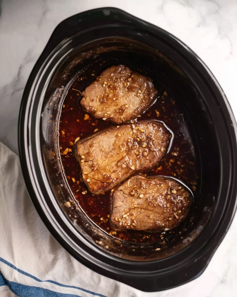 The image shows a black slow cooker filled with three light brown pieces of cooked meat in a dark brown sauce that has small bits of garlic or spices scattered across it. The pieces of meat are arranged in a slightly overlapping manner, fully immersed in the thick sauce. The slow cooker is set on a white marbled surface with a white cloth featuring blue stripes near its edge. Photo taken with an iphone --ar 4:5 --v 7