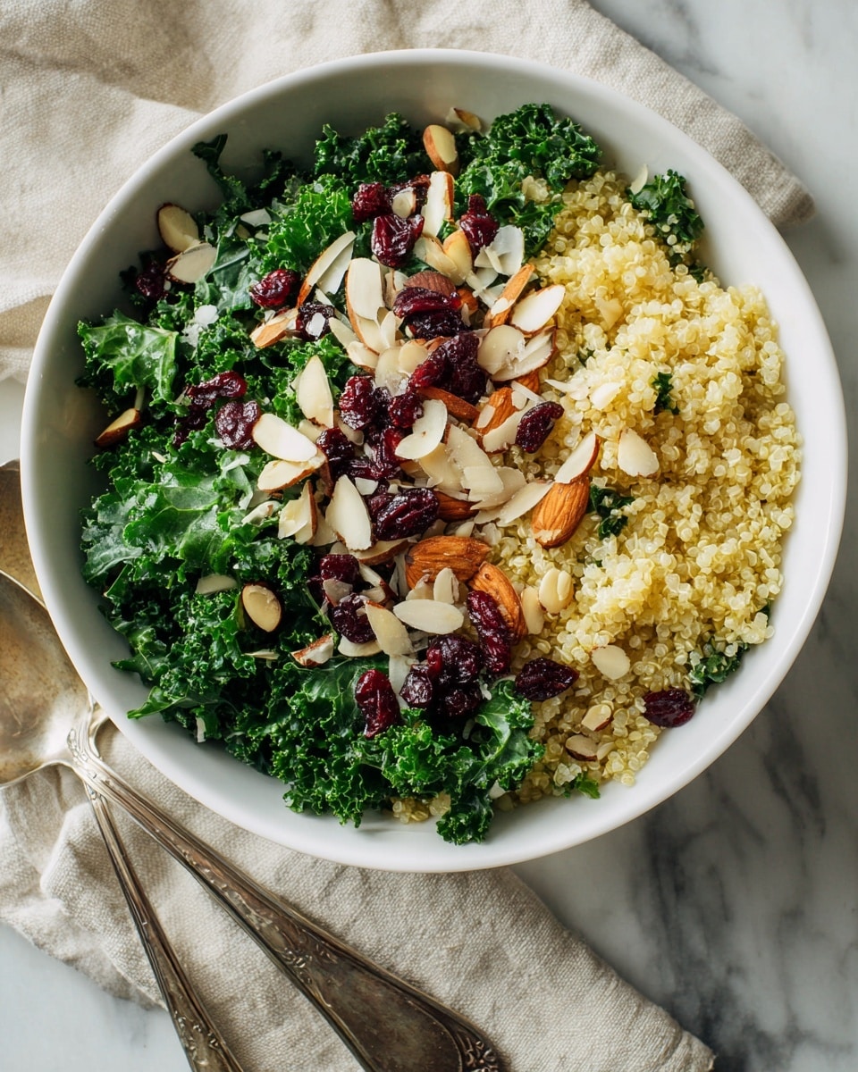 A white bowl filled with a colorful layered salad is placed on a white marbled surface near a beige cloth. The salad has a base layer of bright green chopped kale mixed with light yellow cooked quinoa scattered evenly throughout. On top, there are thin, light brown almond slices and a few scattered deep red dried cranberries, adding texture and color contrast. Next to the bowl, two vintage silver serving utensils rest on the surface. The overall scene is light and natural, showing fresh and healthy ingredients. photo taken with an iphone --ar 4:5 --v 7