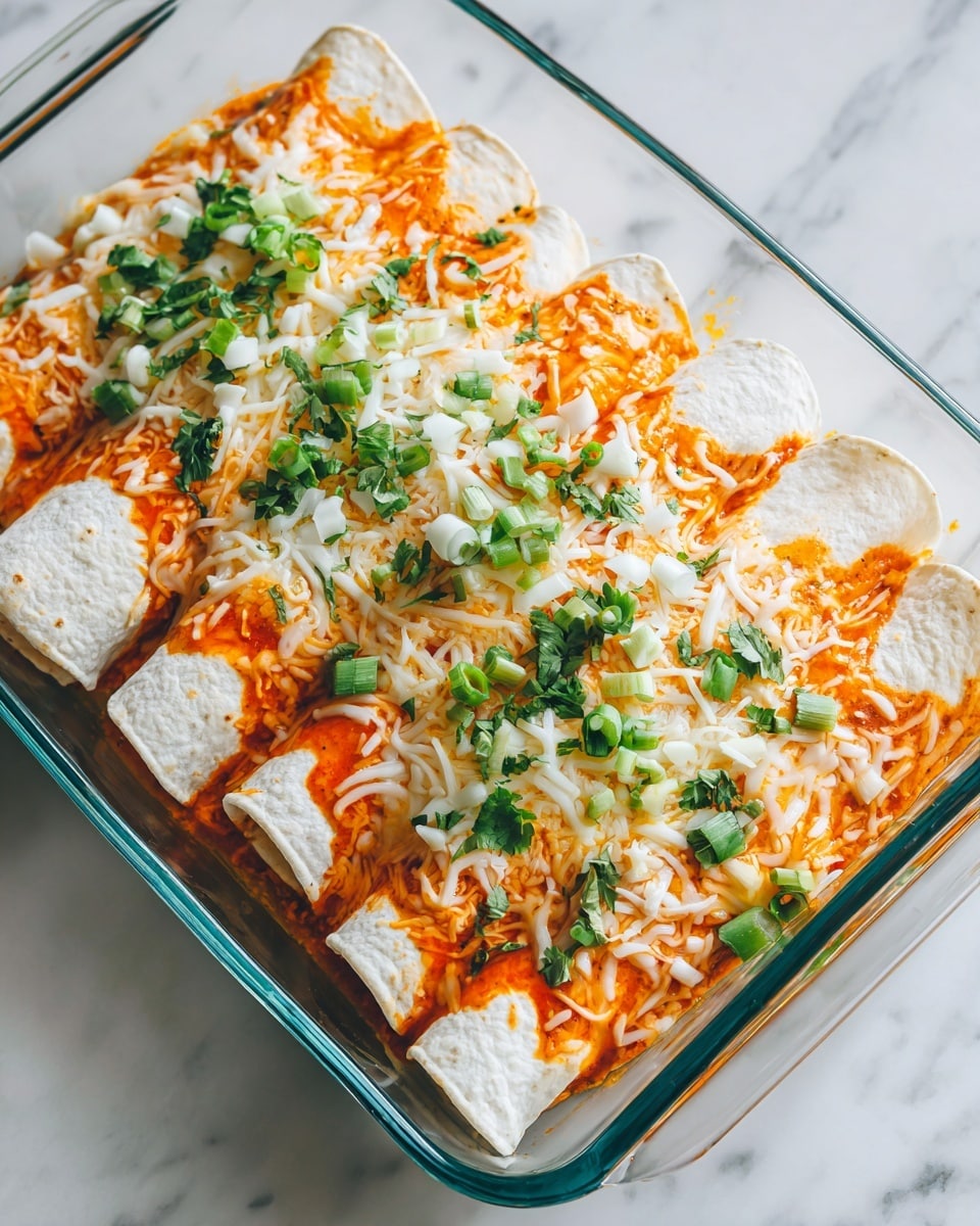 This image shows a clear glass tray on a white marbled surface filled with three layered rolled tortillas. The bottom layer is soft white tortillas, covered by a layer of bright orange sauce that slightly soaks into the tortillas. On top, there is a mix of melted white and yellow cheese that looks smooth and stringy. Fresh green chopped herbs and sliced green onions are scattered evenly over the cheese, adding color contrast. The food looks warm and fresh with a slight glossy shine from melted cheese. Photo taken with an iphone --ar 4:5 --v 7