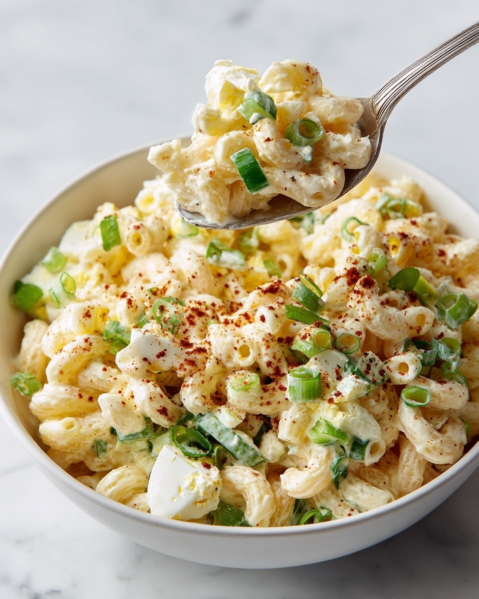 A clear glass bowl on a white marbled surface holds four distinct layers of ingredients arranged side by side. Starting from the right, there is a pile of pale yellow elbow macaroni with a smooth, slightly curved texture. Next to it on the left is a heap of bright white chopped boiled eggs with a rough, chunky texture. Above the eggs is a small pile of finely chopped red onions, showing a mix of white and purple colors with a slightly uneven texture. Next to the onions, at the top, is a pile of chopped green celery with a fresh, crisp look. Nearby on the surface, a small white bowl contains chopped green onions, and fresh whole green onions lie beside it. A blue and white patterned cloth is placed nearby on the surface. Photo taken with an iphone --ar 4:5 --v 7