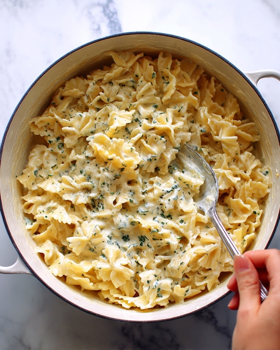 A white bowl filled with a creamy, light yellow pasta that has curly edges and a smooth texture, mixed with small green broccoli florets throughout; a silver fork rests inside the bowl on the left side, with pasta and broccoli stuck to its tines; the pasta is topped with finely grated white cheese and small black pepper specks scattered on top; the bowl is placed on a white marbled surface, and sunlight highlights parts of the dish creating soft shadows; photo taken with an iphone --ar 4:5 --v 7