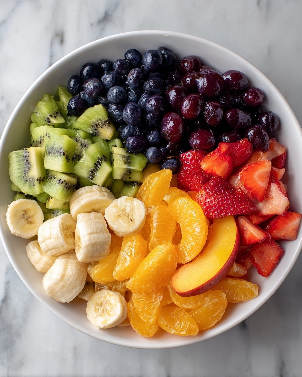 A white bowl filled with six layers of fresh fruit arranged side by side starting from the top left: small dark blue blueberries, diced bright green kiwi, dark red grape halves, sliced light yellow bananas, thin peach slices with a reddish tint near edges, and bright orange mandarin segments mixed with sliced red strawberries. The bowl is placed on a white marbled surface. photo taken with an iphone --ar 4:5 --v 7