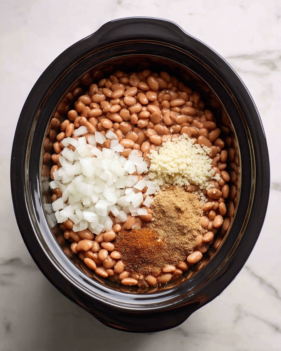 The image shows a black slow cooker filled with four main ingredients in separate layers. The largest layer is a base of light brown pinto beans with small darker spots, covering about half the cooker. On the bottom left, there is a layer of white diced onions, roughly cut into small cubes. On the upper right side, there is a smaller heap of light beige minced garlic. Next to the garlic, there is a heap of light brown ground spices, slightly powdery in texture. The slow cooker is placed on a white marbled surface. photo taken with an iphone --ar 4:5 --v 7