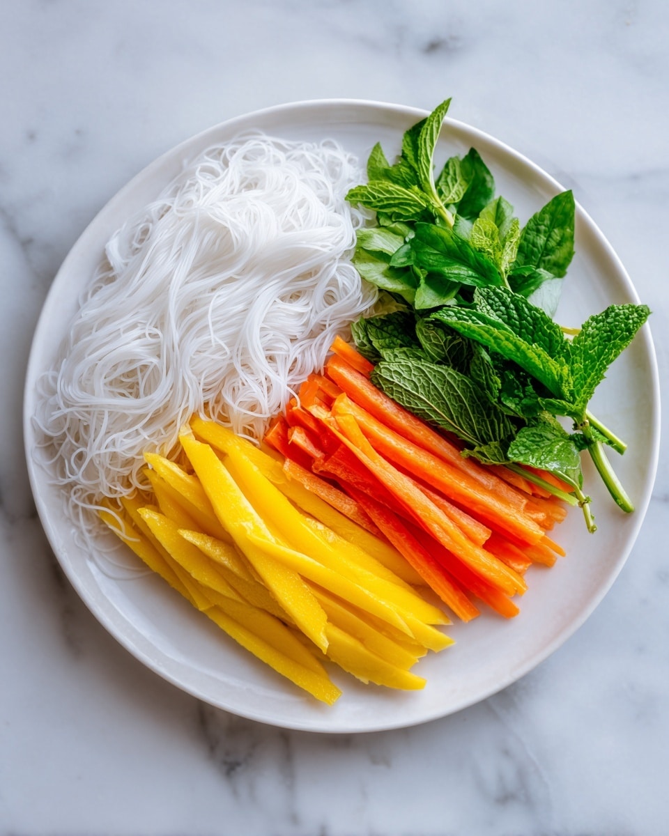 A white plate with a small, neat stack of fresh ingredients in the center consists of three visible layers: the bottom layer is bright yellow mango strips, the middle layer includes orange carrot sticks and some green leafy herbs, and the top layer is a loose pile of translucent white rice noodles. The plate sits on a white marbled surface. Photo taken with an iphone --ar 4:5 --v 7