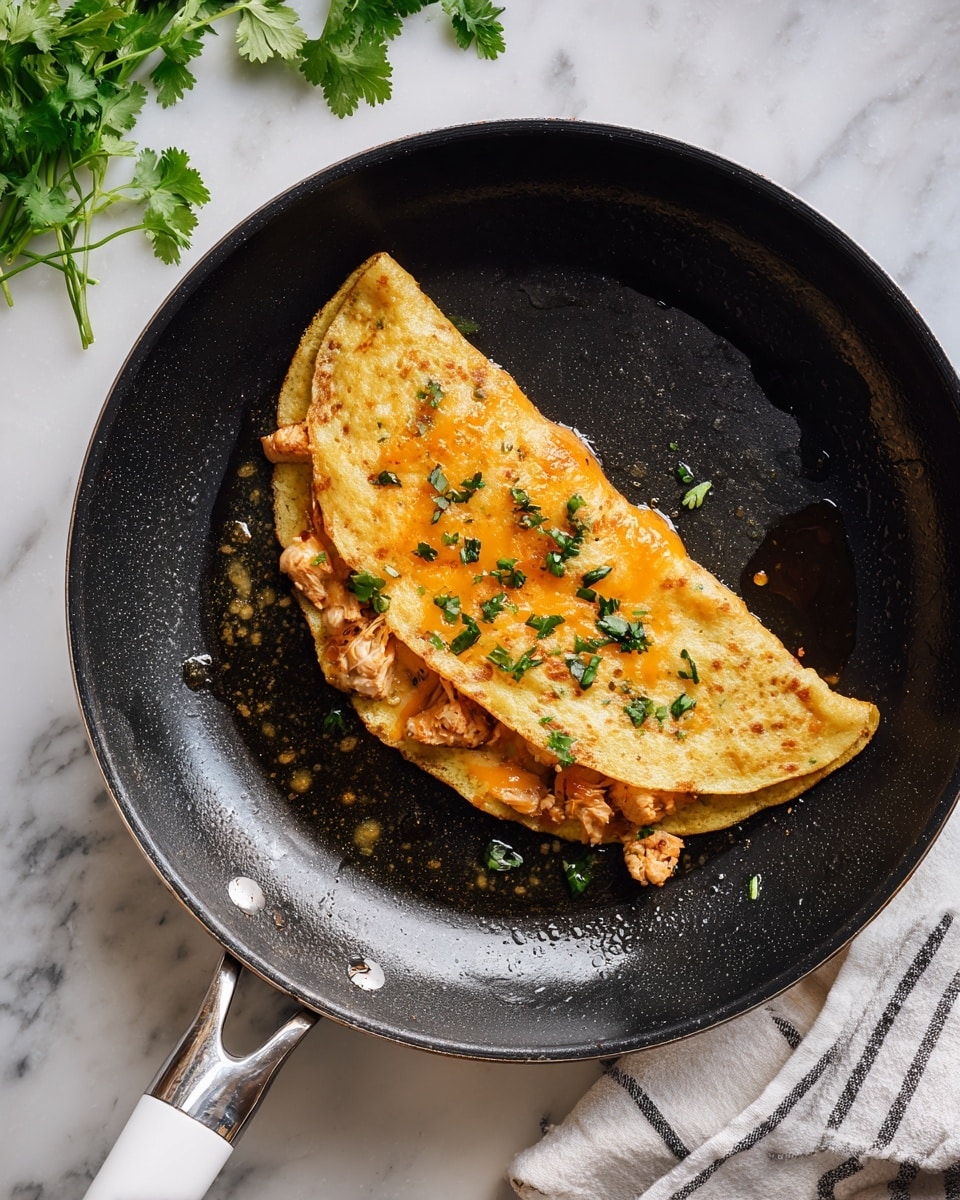 A golden brown folded tortilla filled with a layer of melted bright orange cheese and bits of cooked light brown chicken mixed with green herbs is sizzling in a black frying pan with small oil droplets around. The pan sits on a white marbled surface with a few sprigs of fresh green cilantro above it and a white handle with a striped cloth to the side. Photo taken with an iphone --ar 4:5 --v 7