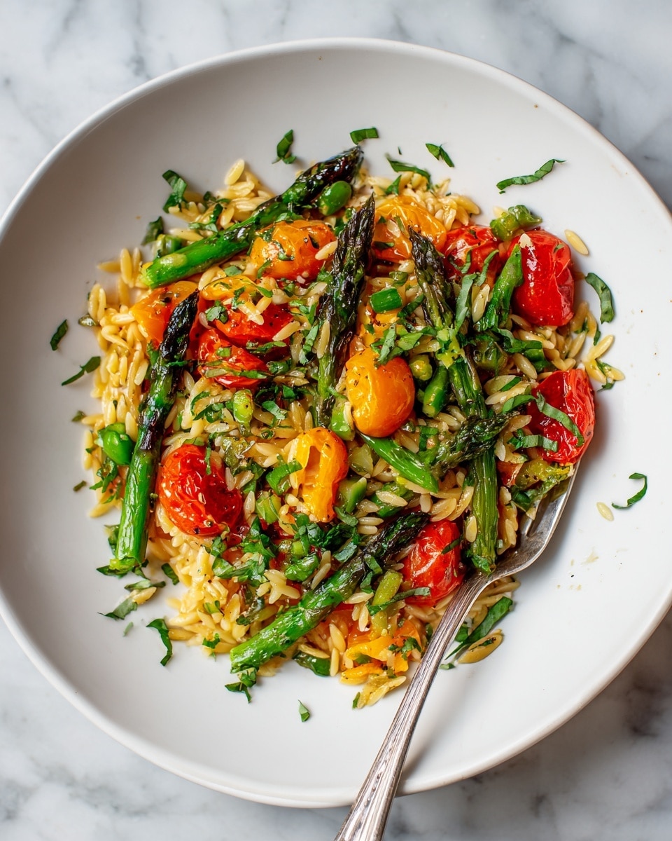 A white plate holds a colorful mixture of cooked small pasta shaped like rice grains, with pieces of bright green asparagus and red and yellow bell peppers scattered throughout. Cherry tomato halves add red pops, while chopped green herbs are sprinkled on top and around the plate edges. A silver fork rests on the right side of the plate, placed on a white marbled surface. photo taken with an iphone --ar 4:5 --v 7