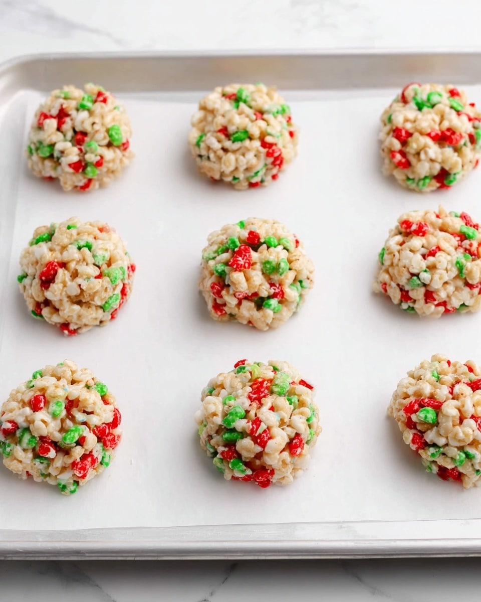 There are eight round, small treats arranged in two rows of four on a white baking tray lined with white parchment paper. Each treat is a textured mix of puffed rice cereal with scattered bright red and green pieces, forming a speckled pattern. The treats have a lumpy, slightly irregular shape with a matte finish. The background is a white marbled surface. photo taken with an iphone --ar 4:5 --v 7