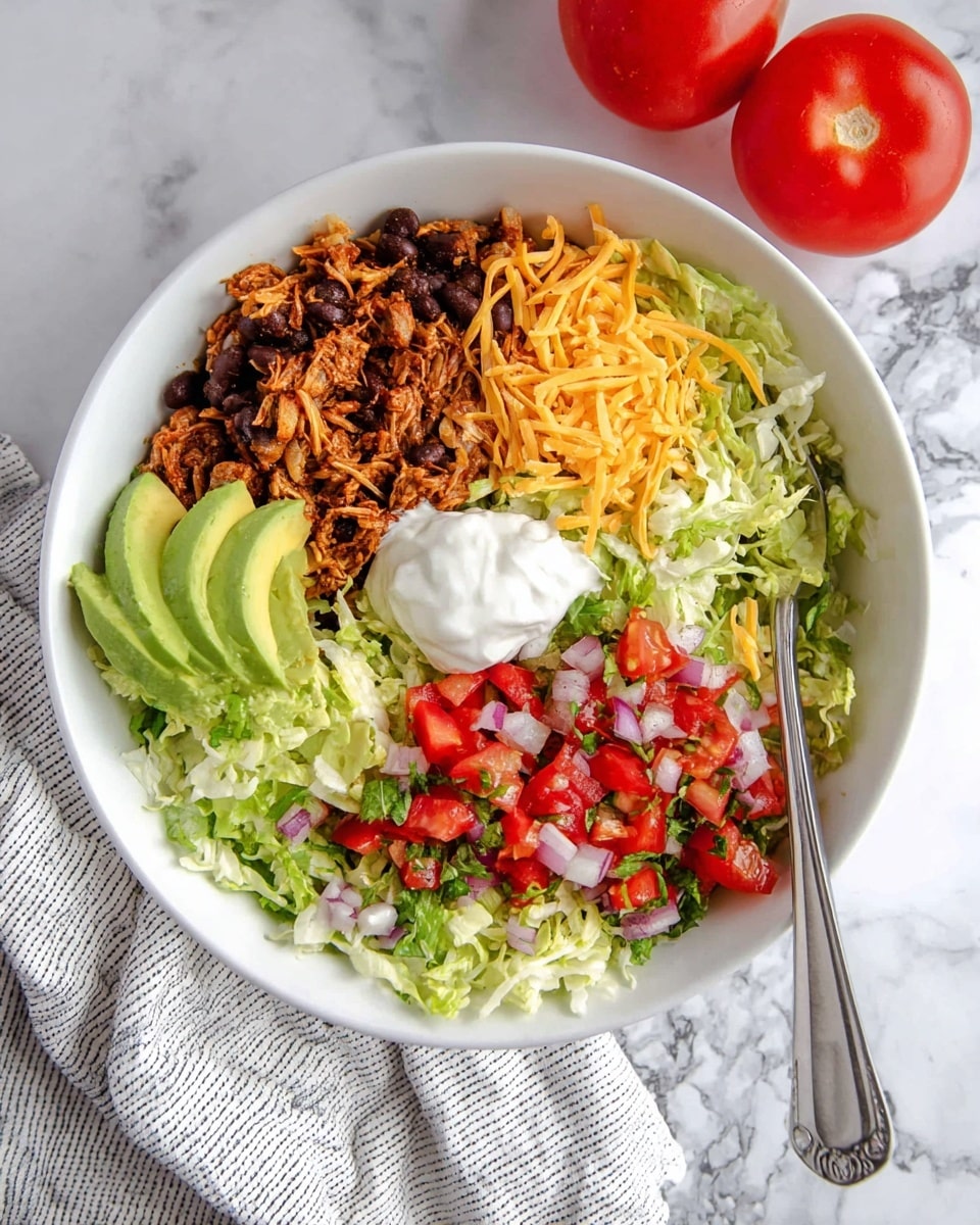 A white bowl contains five visible layers arranged side by side: shredded lettuce with a light green color and crisp texture on the right, diced red tomatoes mixed with finely chopped red onions and some green herbs in the middle right, shredded orange cheddar cheese on the middle left, seasoned shredded dark brown meat with black beans on the far left, and two light green slices of avocado placed above a dollop of smooth white sour cream near the upper center; a silver fork rests on the right side inside the bowl touching the lettuce. The bowl is on a white marbled surface with two ripe red tomatoes on a white and gray striped towel nearby. photo taken with an iphone --ar 4:5 --v 7