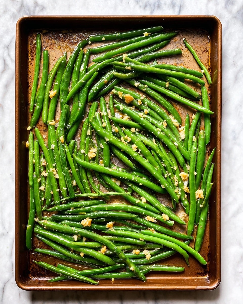 A rectangular baking tray filled with cooked green beans spread evenly across the entire surface. The green beans are vibrant, long, and slender, coated with small bits of chopped garlic and pieces of onions scattered lightly over them. The tray surface is a dark bronze color, contrasting with the bright green of the beans. The background is a white marbled surface that adds a clean and fresh look to the scene. The lighting highlights the fresh texture and slight shine on the beans. photo taken with an iphone --ar 4:5 --v 7