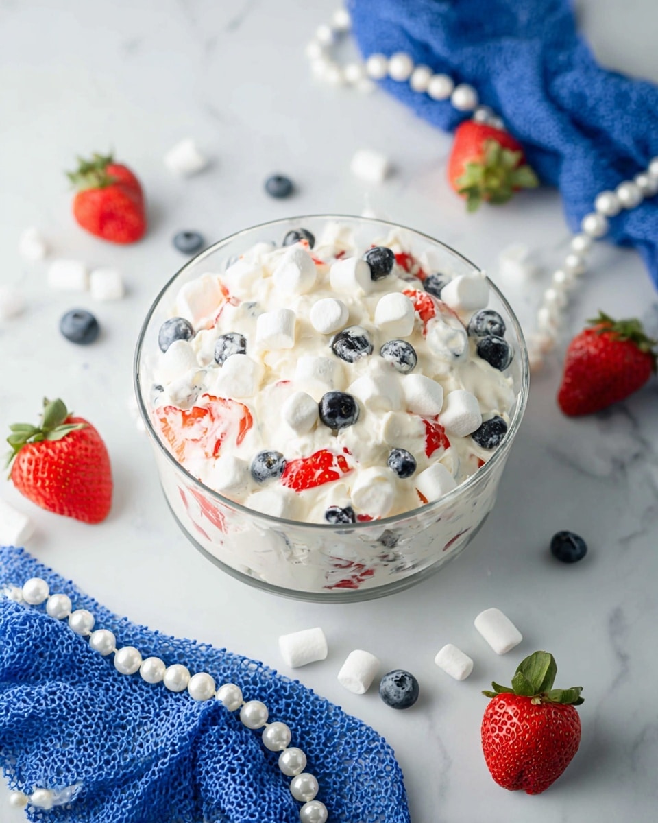 A clear glass bowl is filled with a creamy white mixture that looks light and fluffy. Mixed inside are visible pieces of red strawberries and small dark blueberries, giving pops of color throughout the creamy texture. The bowl sits on a white marbled surface, and the mixture has a soft, whipped look with some fruit pieces partially covered by the cream. Photo taken with an iphone --ar 4:5 --v 7