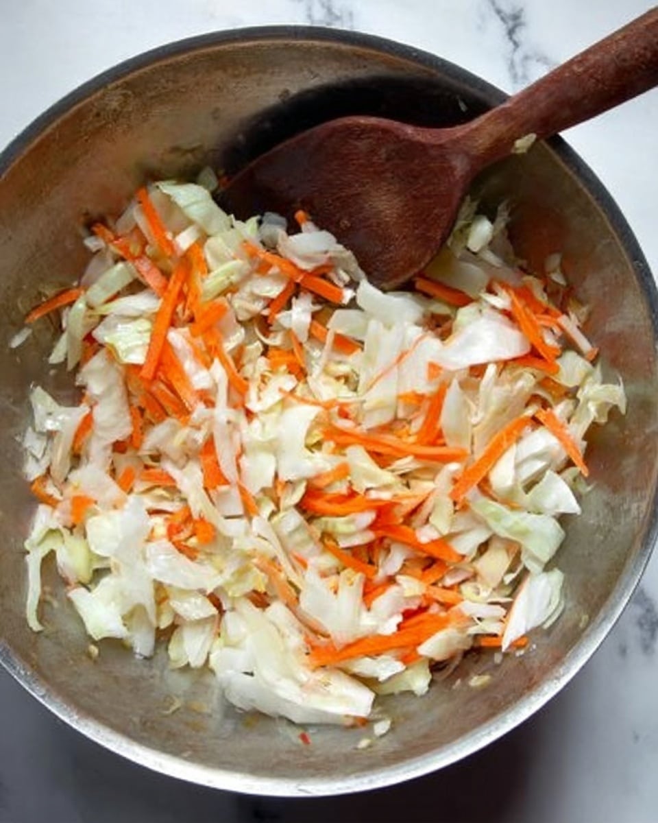 A metal bowl filled with chopped vegetables, mainly white cabbage pieces and thin orange carrot strips. A wooden spoon is resting inside the bowl, stirring the vegetables. The background is a white marbled surface. Photo taken with an iphone --ar 4:5 --v 7