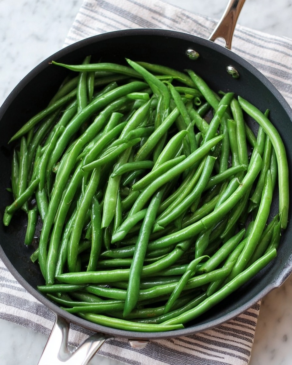 A black pan filled with many bright green long beans that are shiny and fresh, covering the whole pan evenly in one layer with different angles and slight curves. The pan is placed on a white marbled surface with a striped cloth underneath the pan handle. Photo taken with an iphone --ar 4:5 --v 7