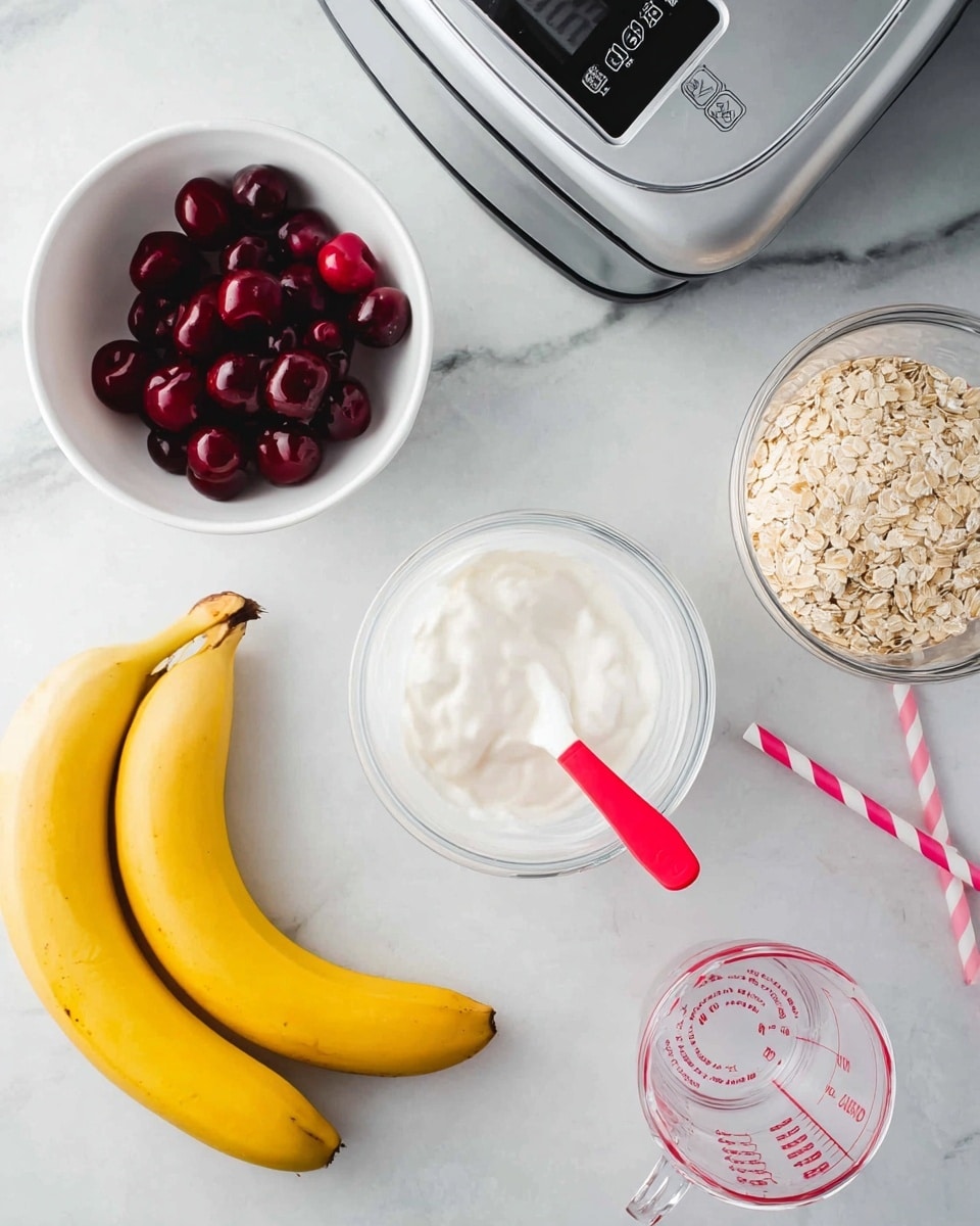 The image shows several food items and kitchen tools on a white marbled surface. On the top left, there is a white bowl filled with dark red cherries. Below the bowl is a white container of creamy white yogurt with a spoon that has a bright red handle inside it. Toward the bottom left corner, three yellow bananas are seen. At the center right, there is a clear glass jar filled with rolled oats. On the far right side, a silver KitchenAid blender base with black control buttons is partially visible. In the bottom right corner, there is a clear glass measuring cup with red markings. Two pink and white striped paper straws lie on the surface near the bowl of cherries. Photo taken with an iphone --ar 4:5 --v 7